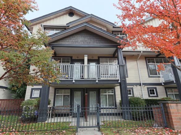 Modern multi-family townhouse with spacious balconies and a contemporary design in an urban setting. The property features elegant siding, large windows, and is surrounded by beautifully maintained landscaping with autumn foliage.