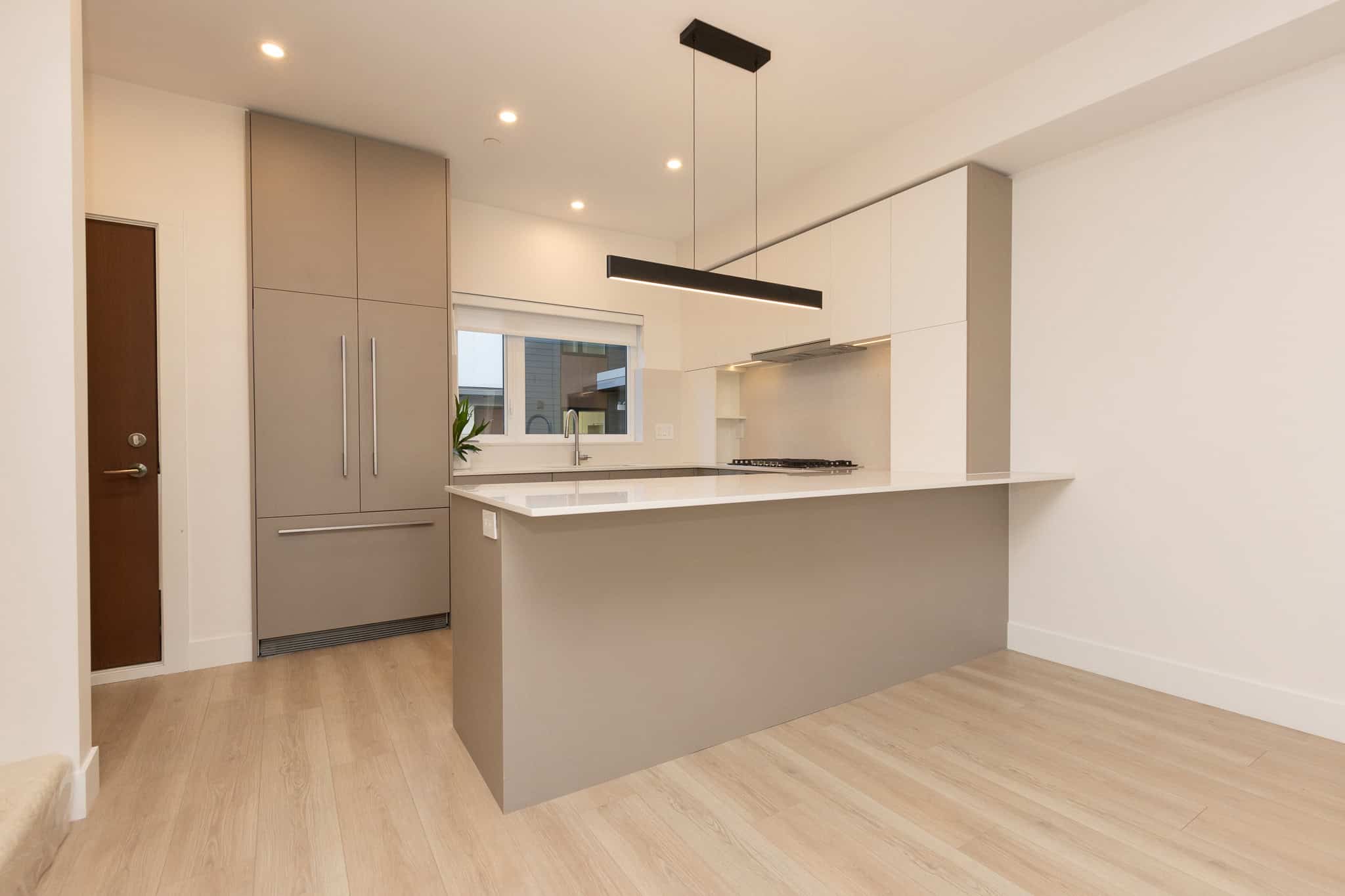 Modern kitchen with grey and white cabinetry, quartz countertops, stainless steel appliances, and a sleek black pendant light, showcasing contemporary condo living at Orca Realty Inc.