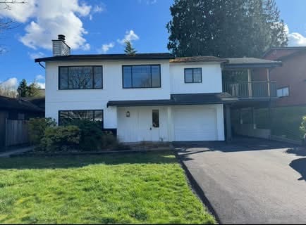 Spacious two-story house with large windows and a garage, situated on a green lawn with clear blue skies in the background, perfect for family living and real estate investment.