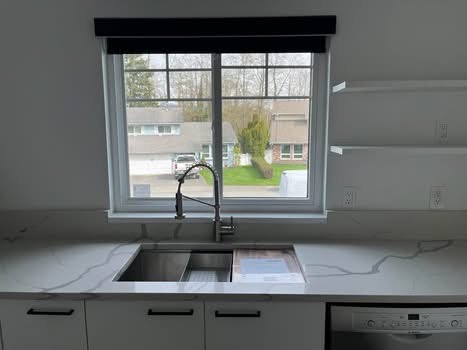 Modern kitchen sink with marble countertop and large window showcasing a residential neighbourhood in Victoria BC.