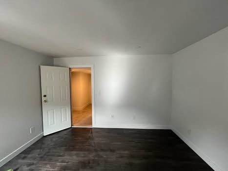 Bright empty living room with white walls, dark hardwood floors, and an open door leading to a hallway. Ideal for real estate listings showcasing modern interior spaces in Vancouver.
