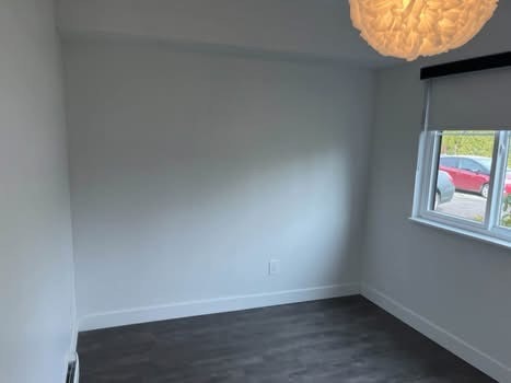 Bright empty bedroom with white walls, large window, and modern dark flooring, ideal for homebuyers and real estate listings in British Columbia.
