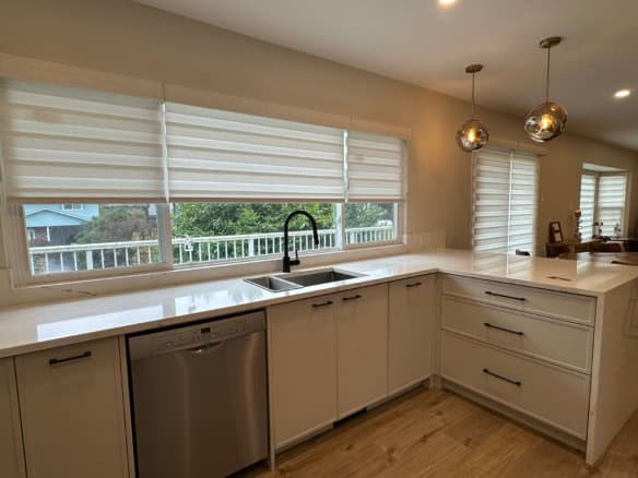Bright modern kitchen with large window, white cabinetry, marble countertops, stainless steel dishwasher, and stylish pendant lighting - perfect for Vancouver homebuyers.