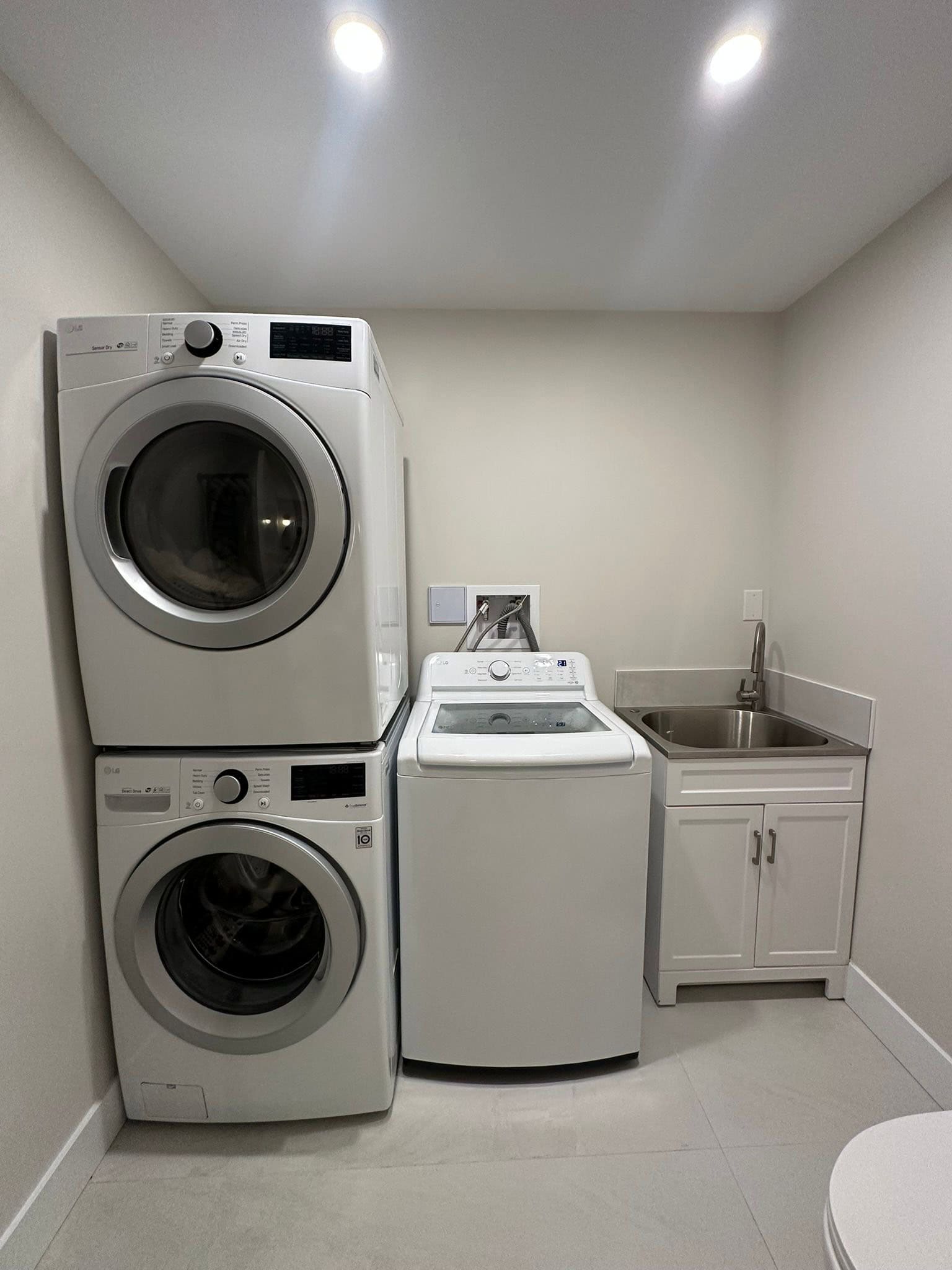 Bright laundry room with washer, dryer, utility sink, and storage cabinets, ideal for residential or commercial property. Showcasing modern appliances in a clean, functional space.