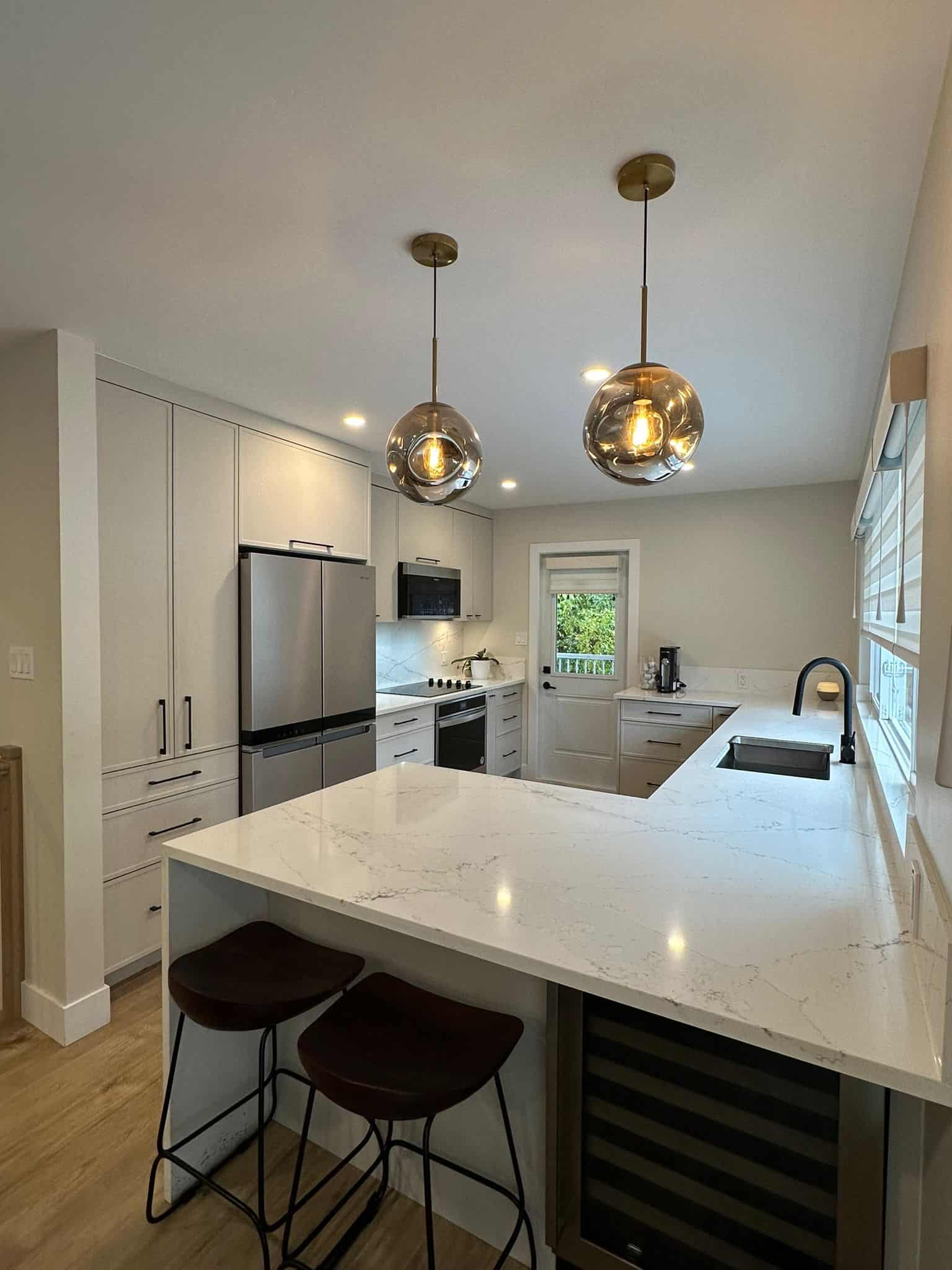 Modern kitchen with white cabinets, marble island, stainless steel appliances, and cozy lighting fixtures, perfect for Vancouver Island homebuyers searching for stylish real estate.