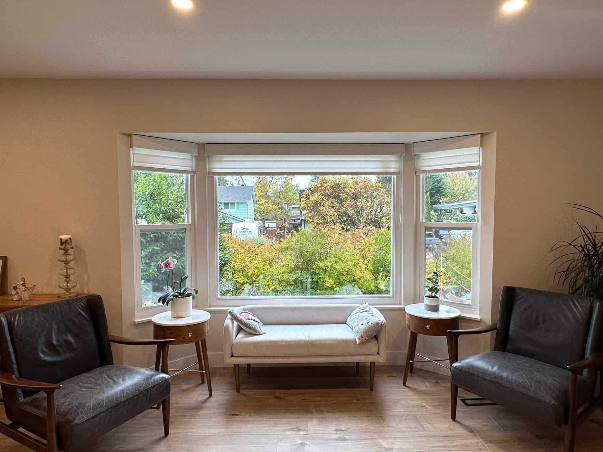 Bright living room with large bay window showcasing lush greenery view; cozy seating area featuring modern decor and natural light, ideal for relaxing and enjoying the scenic surroundings.