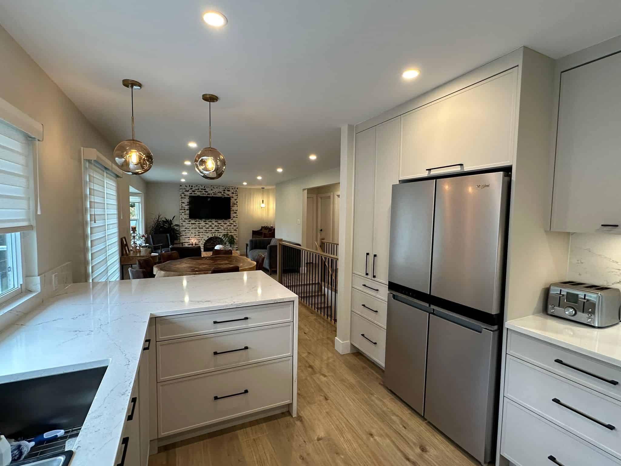 Modern kitchen and open-concept living space with stainless steel appliances, white cabinetry, and elegant lighting, perfect for Vancouver homebuyers and real estate investors.