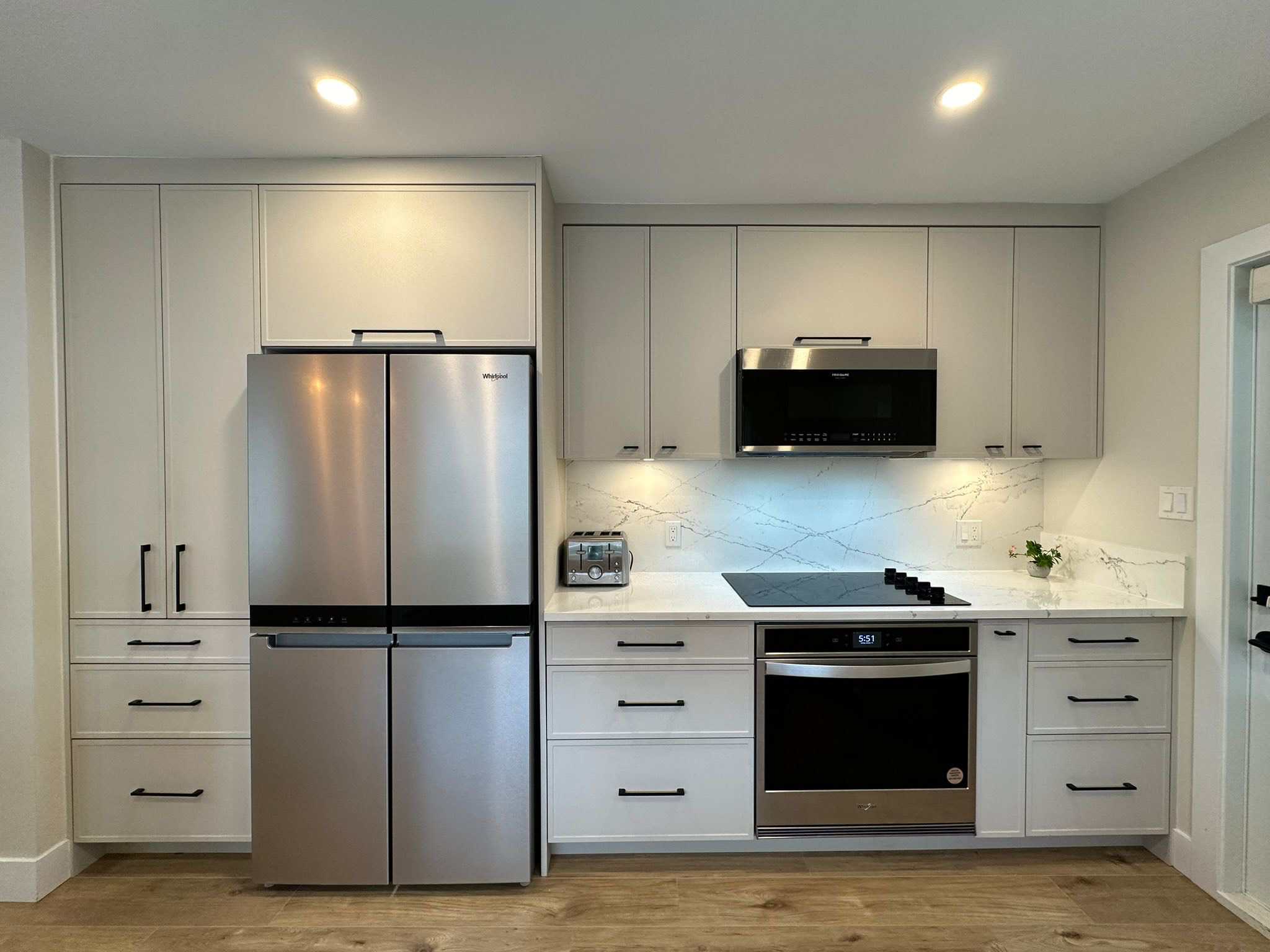 Modern kitchen with stainless steel refrigerator, oven, and microwave, featuring sleek white cabinetry and a stylish marble backsplash, ideal for Vancouver real estate listings.
