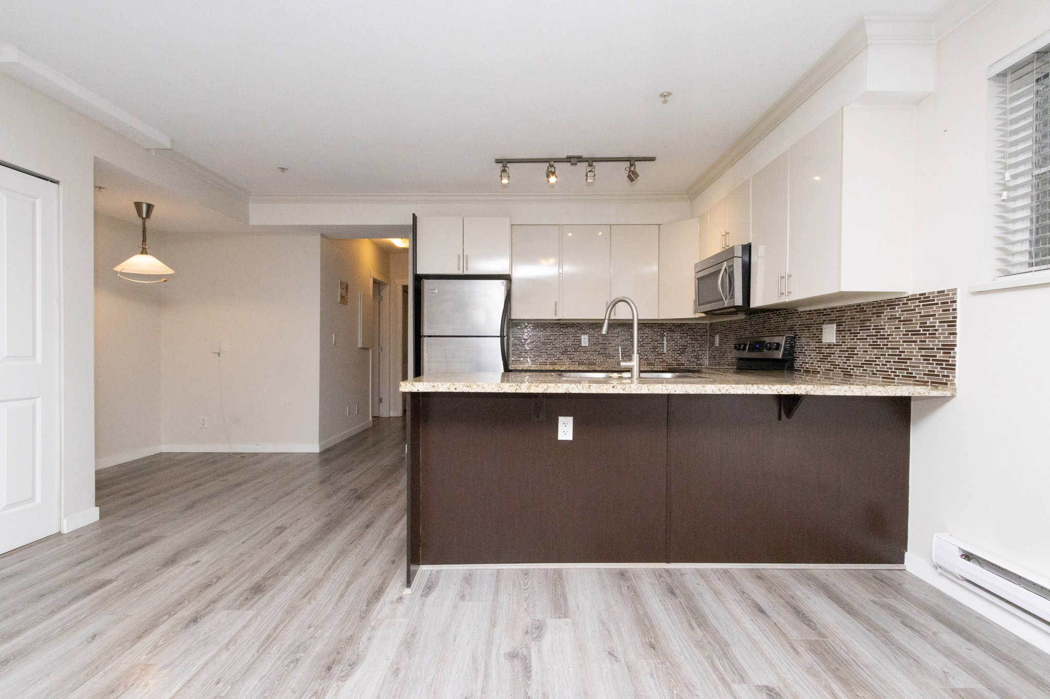 Bright modern kitchen with white cabinets, granite countertops, stainless steel appliances, and a stylish brown tile backsplash in an upscale Orca Realty Canada property.