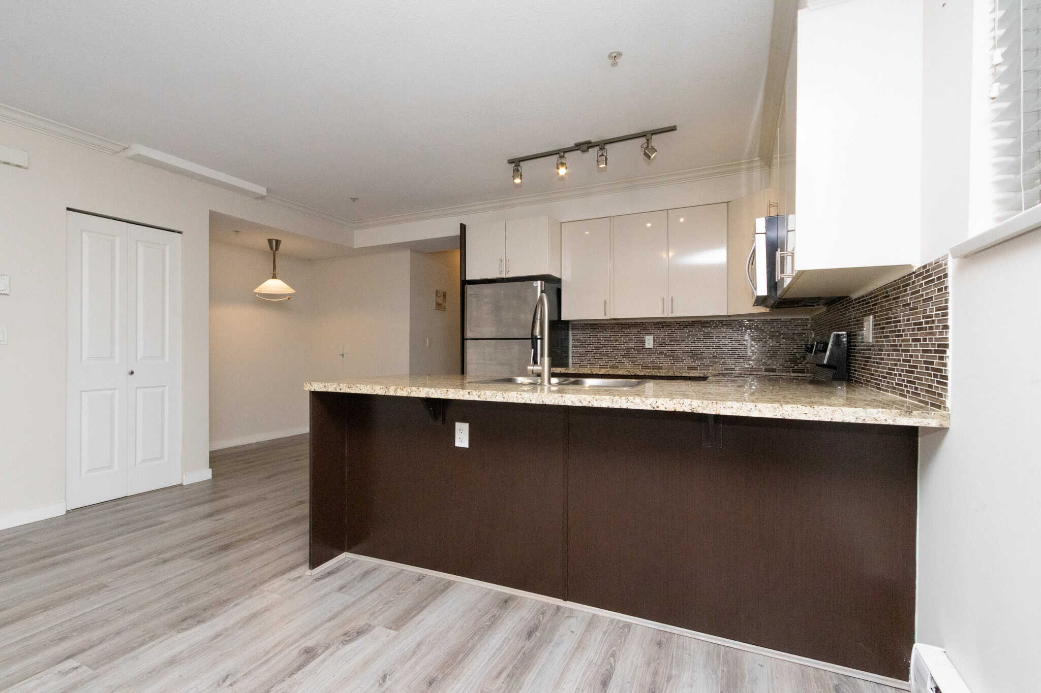 Modern kitchen with granite countertops, white cabinetry, stainless steel appliances, and a mosaic tile backsplash in a contemporary condo. Perfect for comfortable living and entertaining.