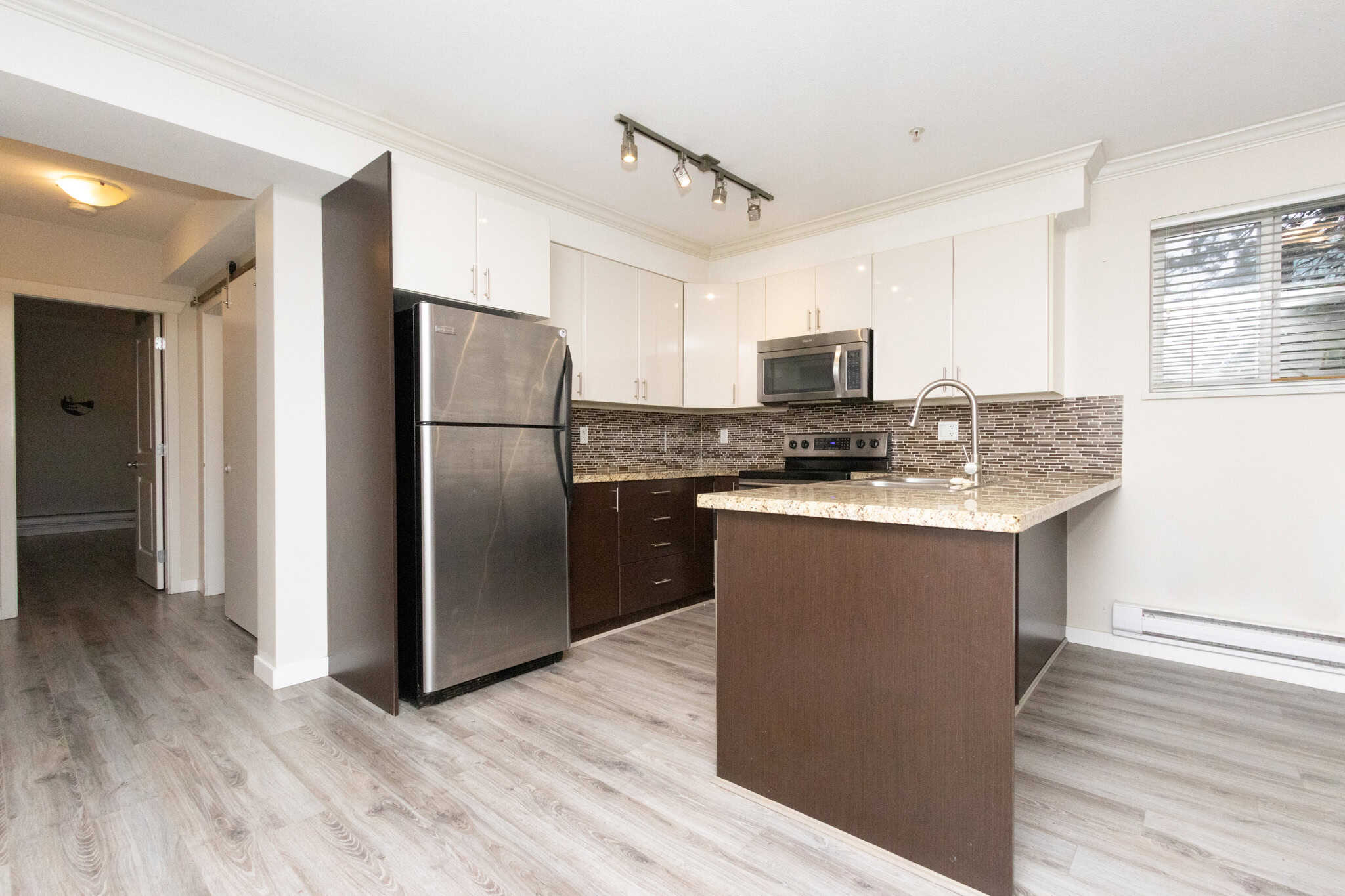 Modern kitchen with stainless steel appliances, white and dark brown cabinetry, granite countertops, and a contemporary backsplash in Orca Realty Inc. listing.