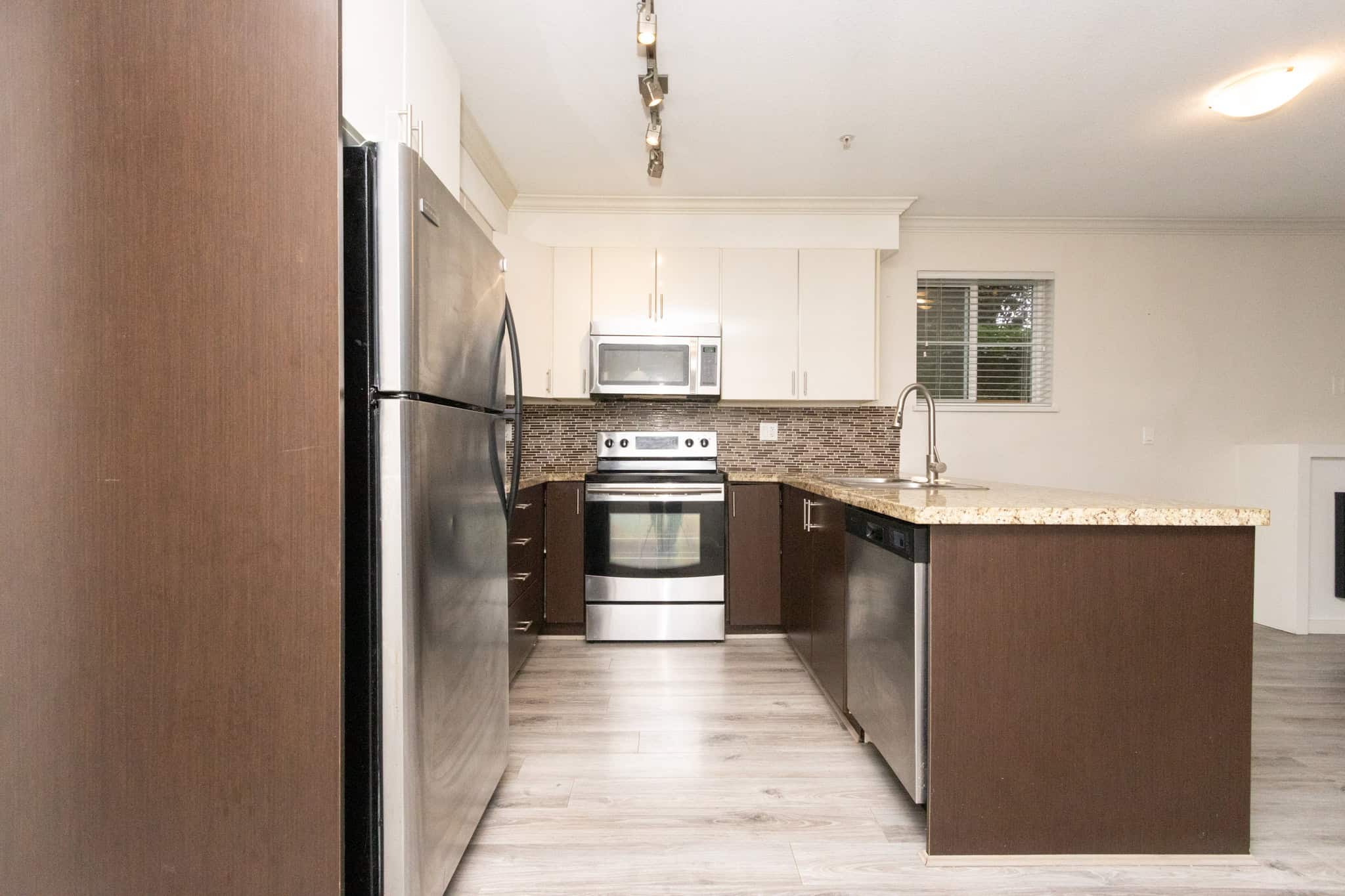 Stainless steel kitchen appliances with modern white cabinetry, granite countertops, and a tiled backsplash in a contemporary home listed by Orca Realty Inc., Vancouver, BC.