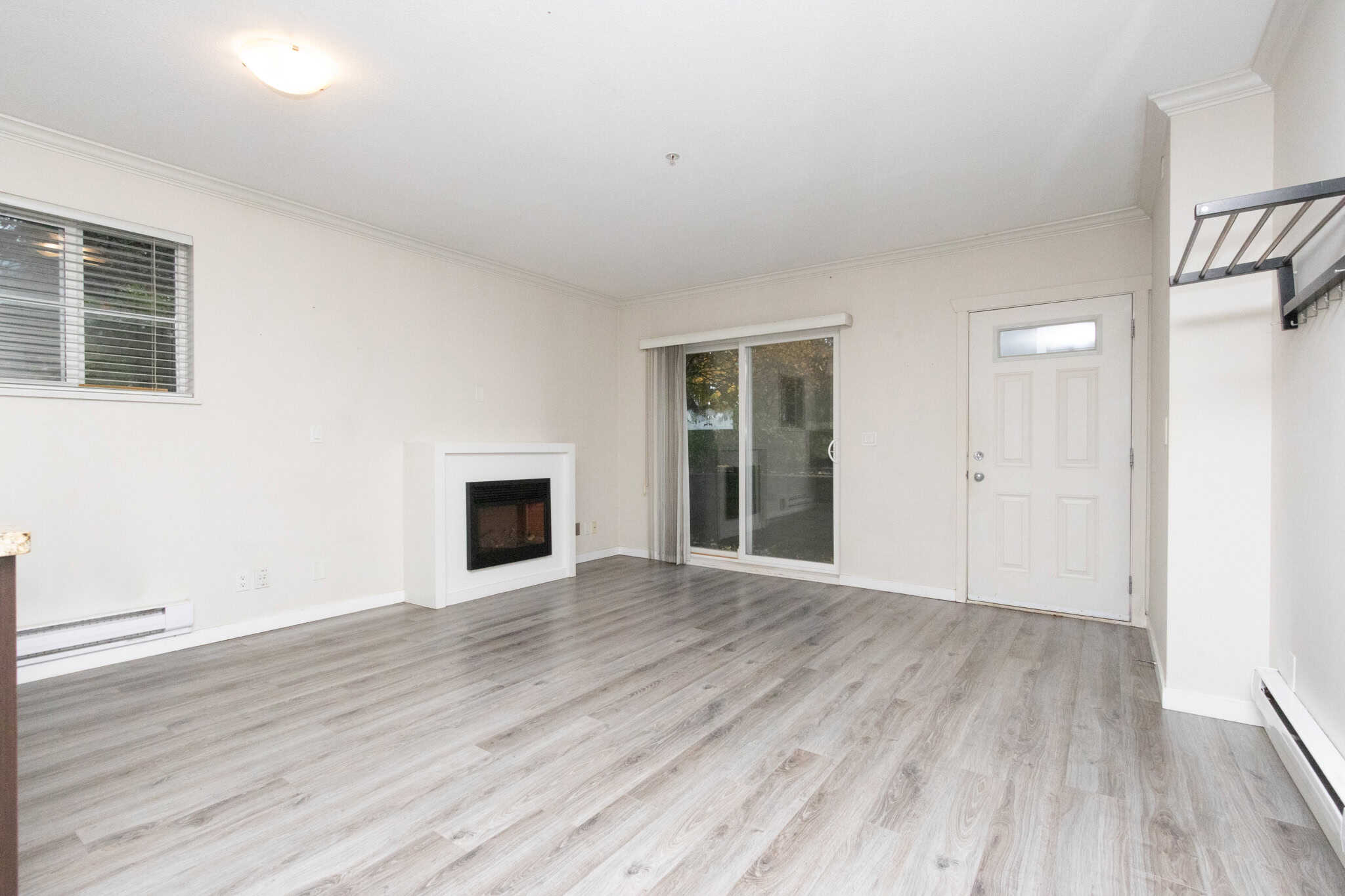 Spacious living room with modern laminate flooring, fireplace, sliding glass door leading to outdoors, and neutral wall colours, ideal for Vancouver real estate buyers.