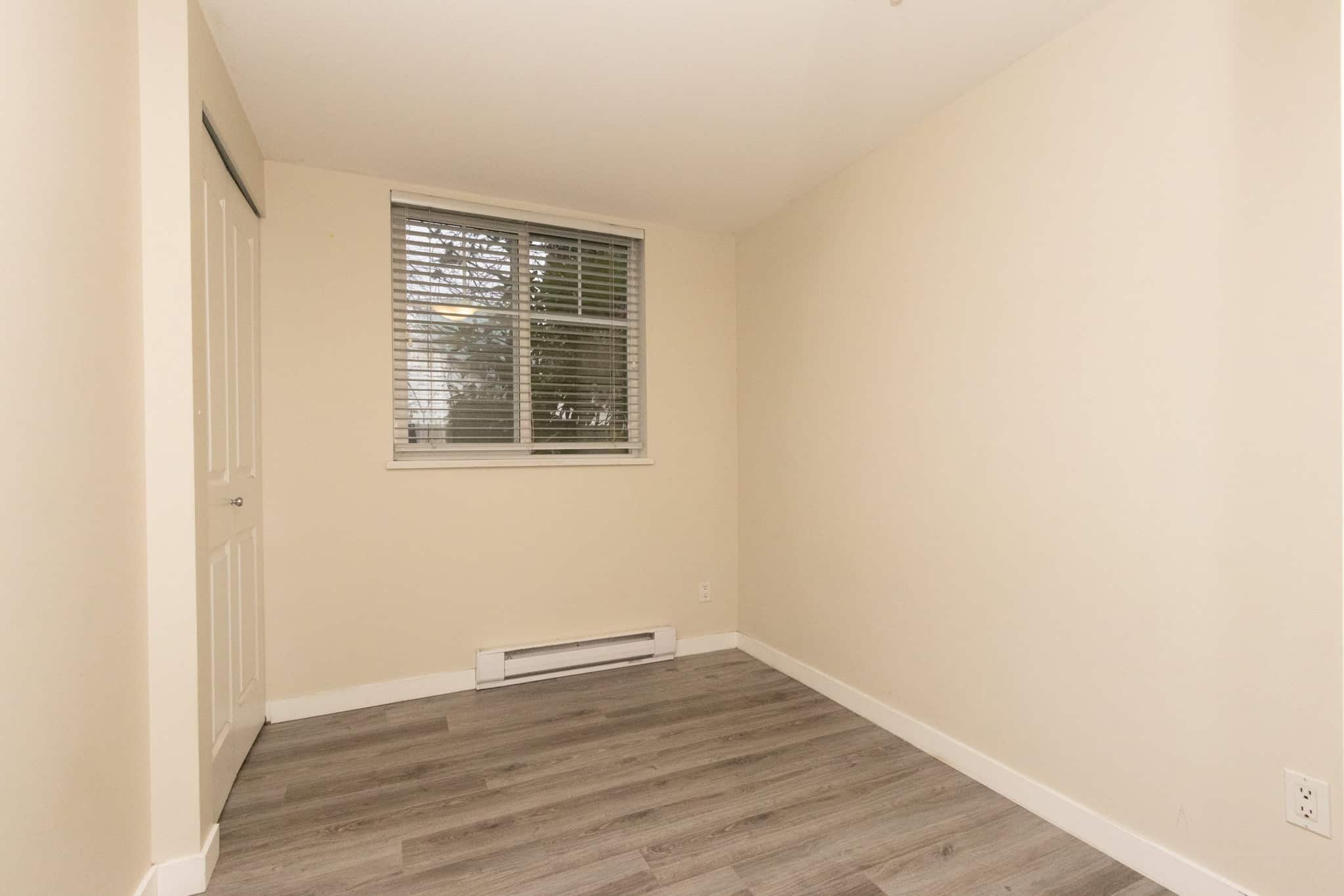 Bright empty room with beige walls and laminate flooring, featuring a window with blinds and a closet, ideal for real estate listings by Orca Realty Inc.
