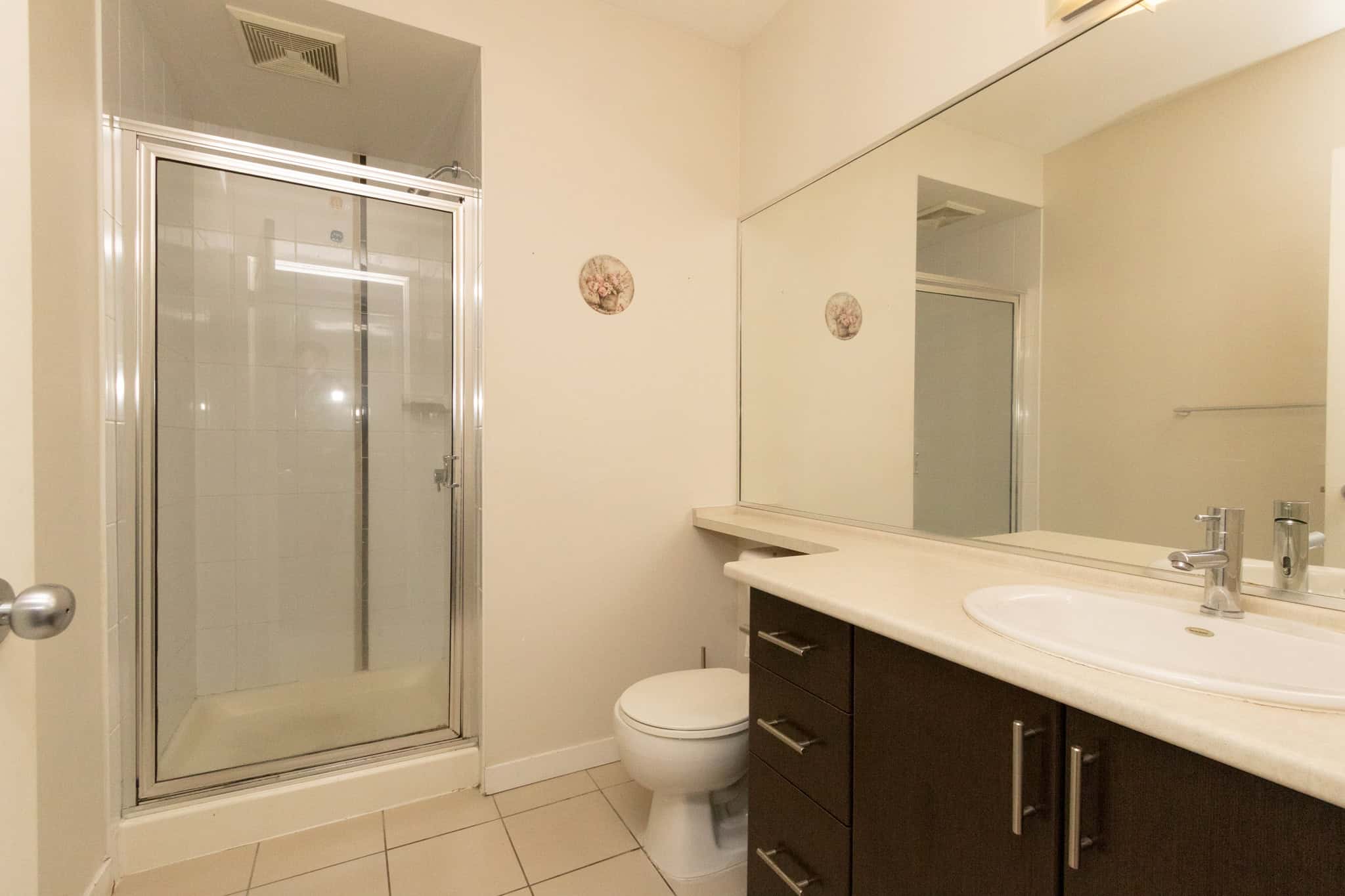Bright bathroom with glass shower, modern vanity with storage, large mirror, and neutral tones, perfect for short-term or long-term rental property in Victoria, BC.