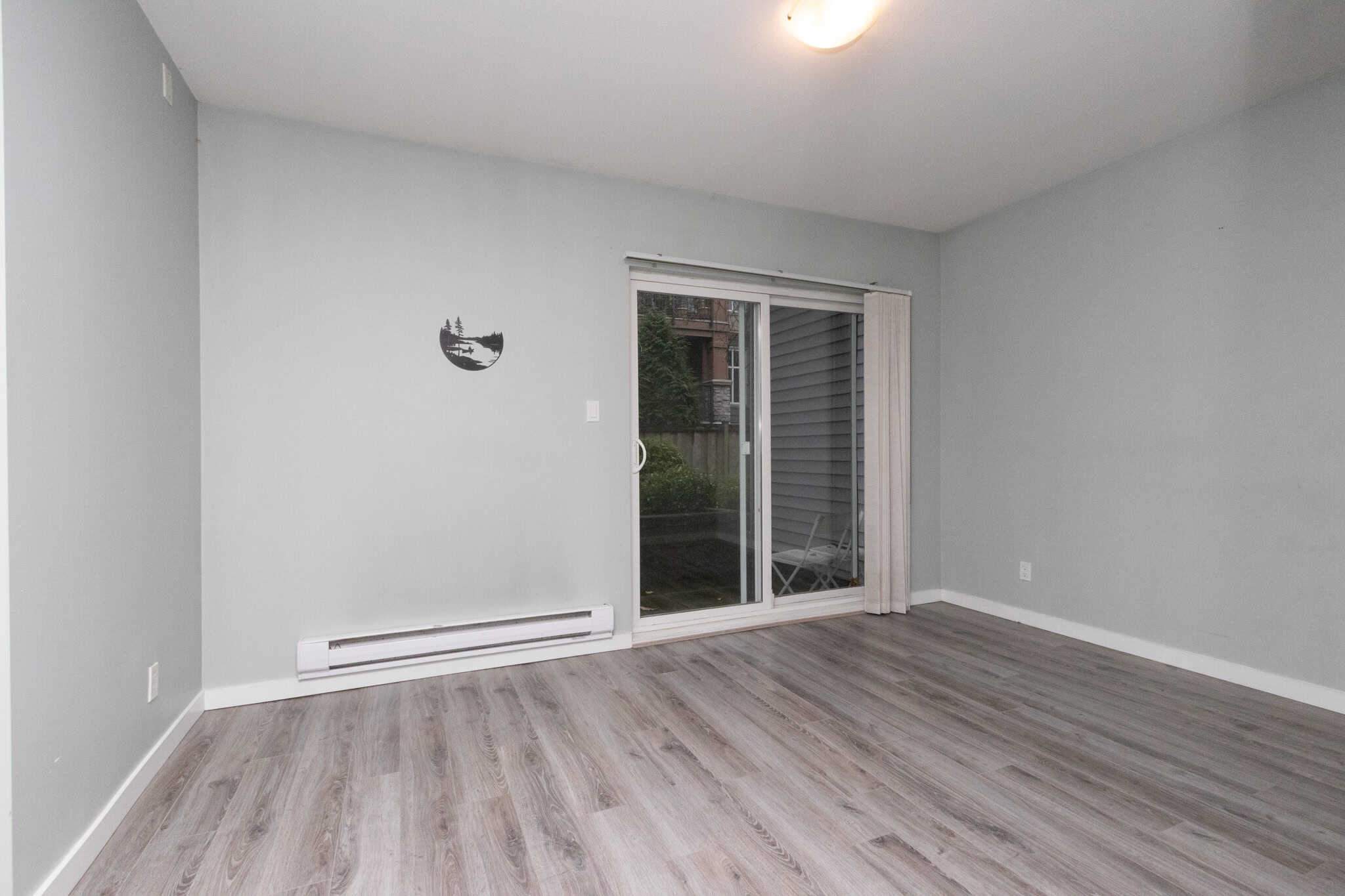 Bright, welcoming living room with sliding glass door to outdoor patio, featuring neutral wall colours and laminate flooring, ideal for property buyers and real estate investors in Canada.