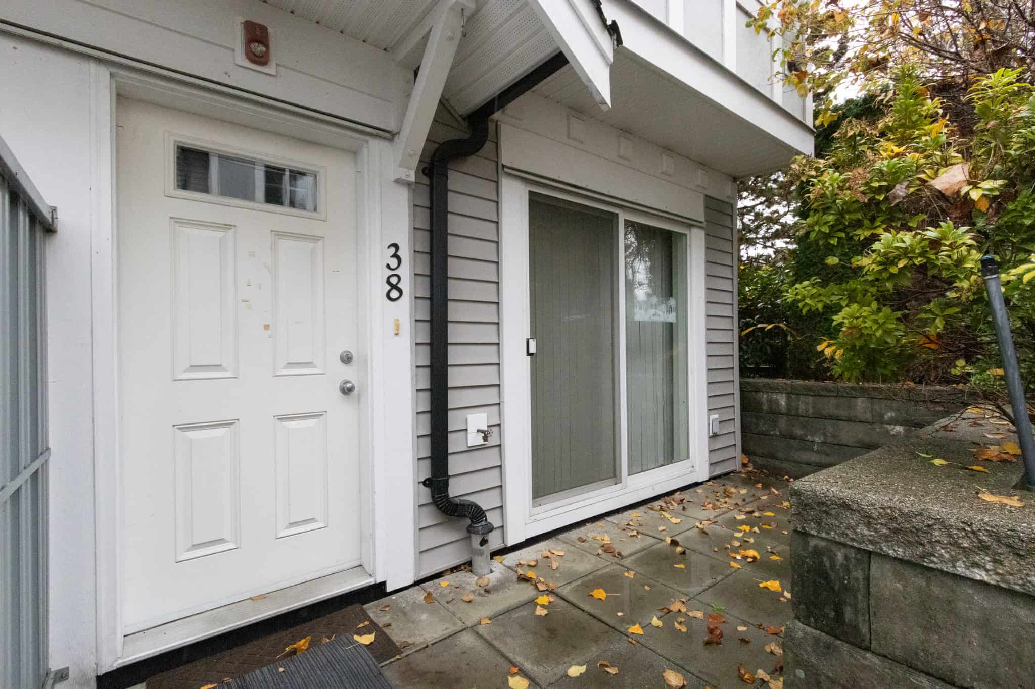 Bright Vancouver Island home entrance with white door and sliding glass door, surrounded by lush greenery, perfect for real estate listings and showcasing local property features in Victoria, BC.