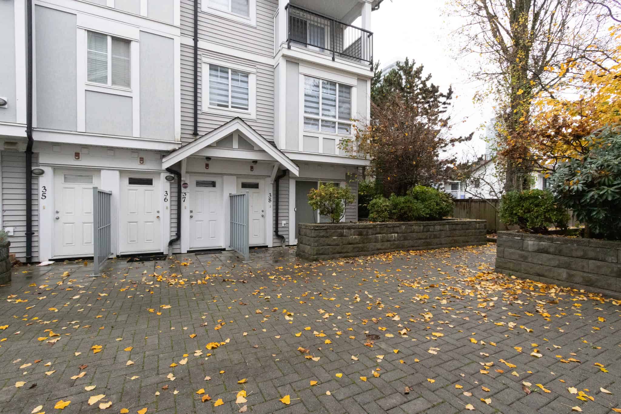 Modern townhouse entrance with secure white doors, surrounded by autumn foliage and paved walkway, representing Orca Realty Inc.'s professional property management and real estate services in Vancouver.
