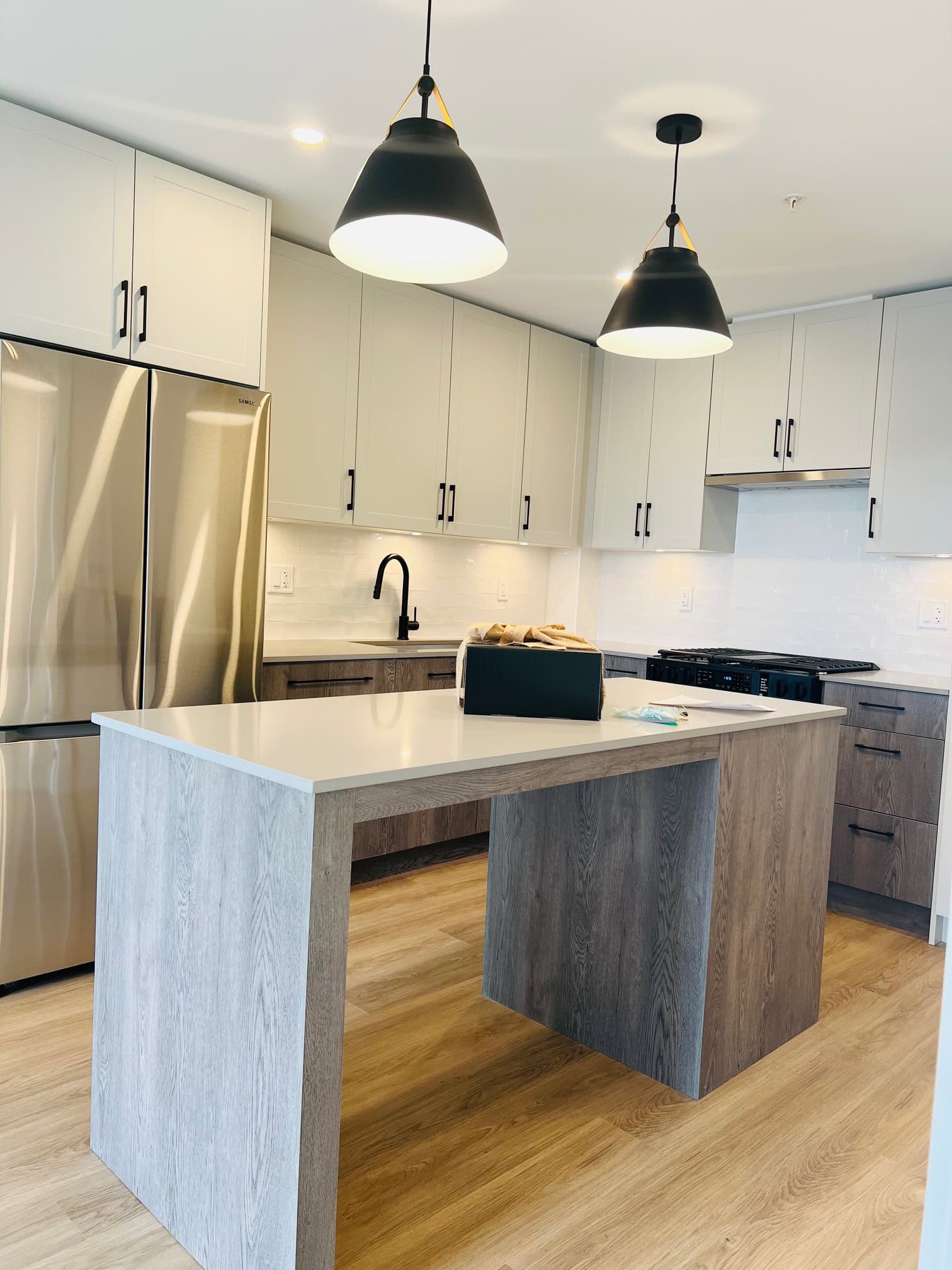 IMG_5600 Bright modern kitchen with white cabinetry, black hardware, stainless steel appliances, and a kitchen island with a natural wood finish, perfect for contemporary living.