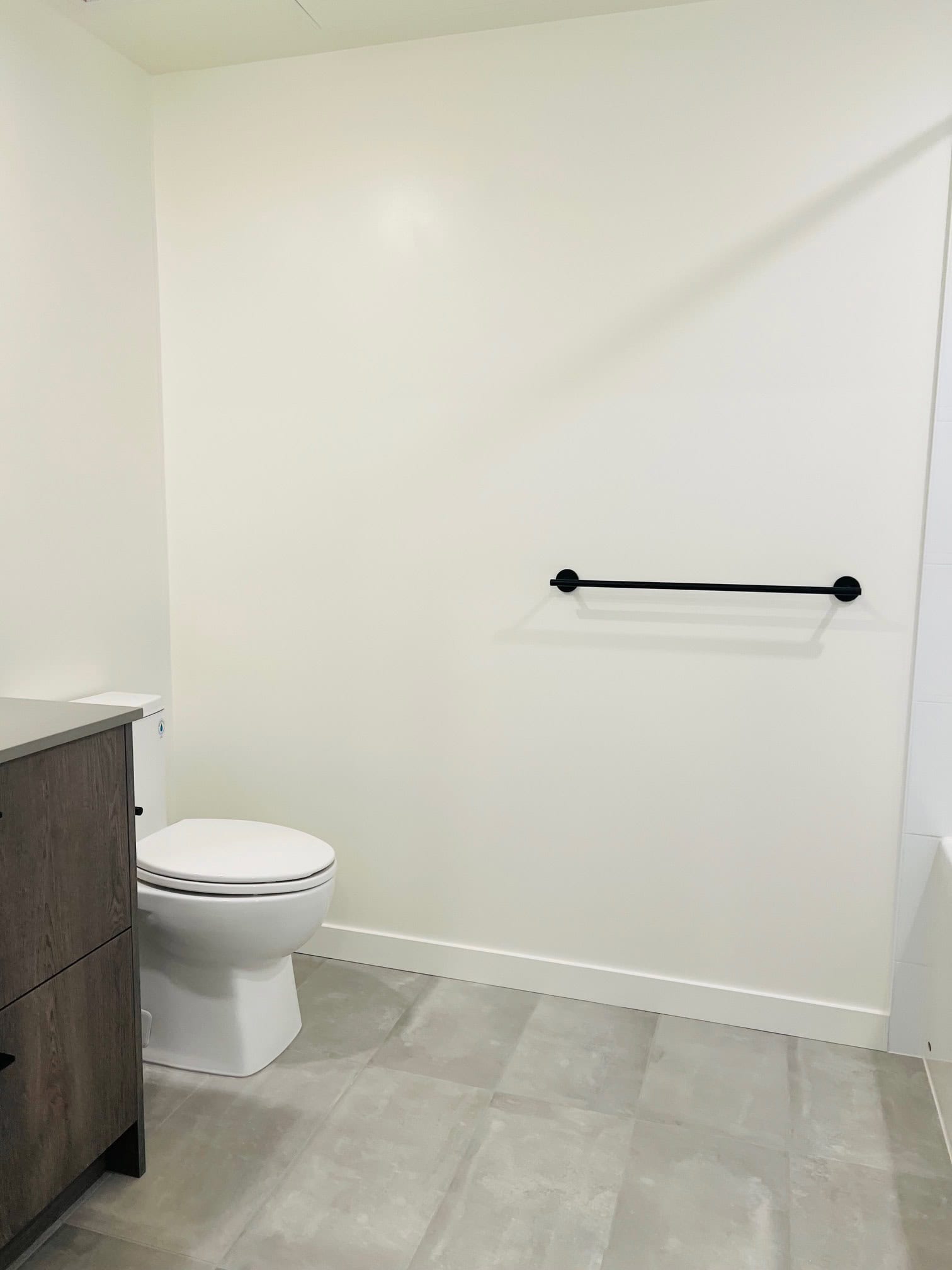 IMG_5603 Modern bathroom interior with white walls, toilet, black towel bar, and tiled flooring, showcasing contemporary condo or residential design in Vancouver.