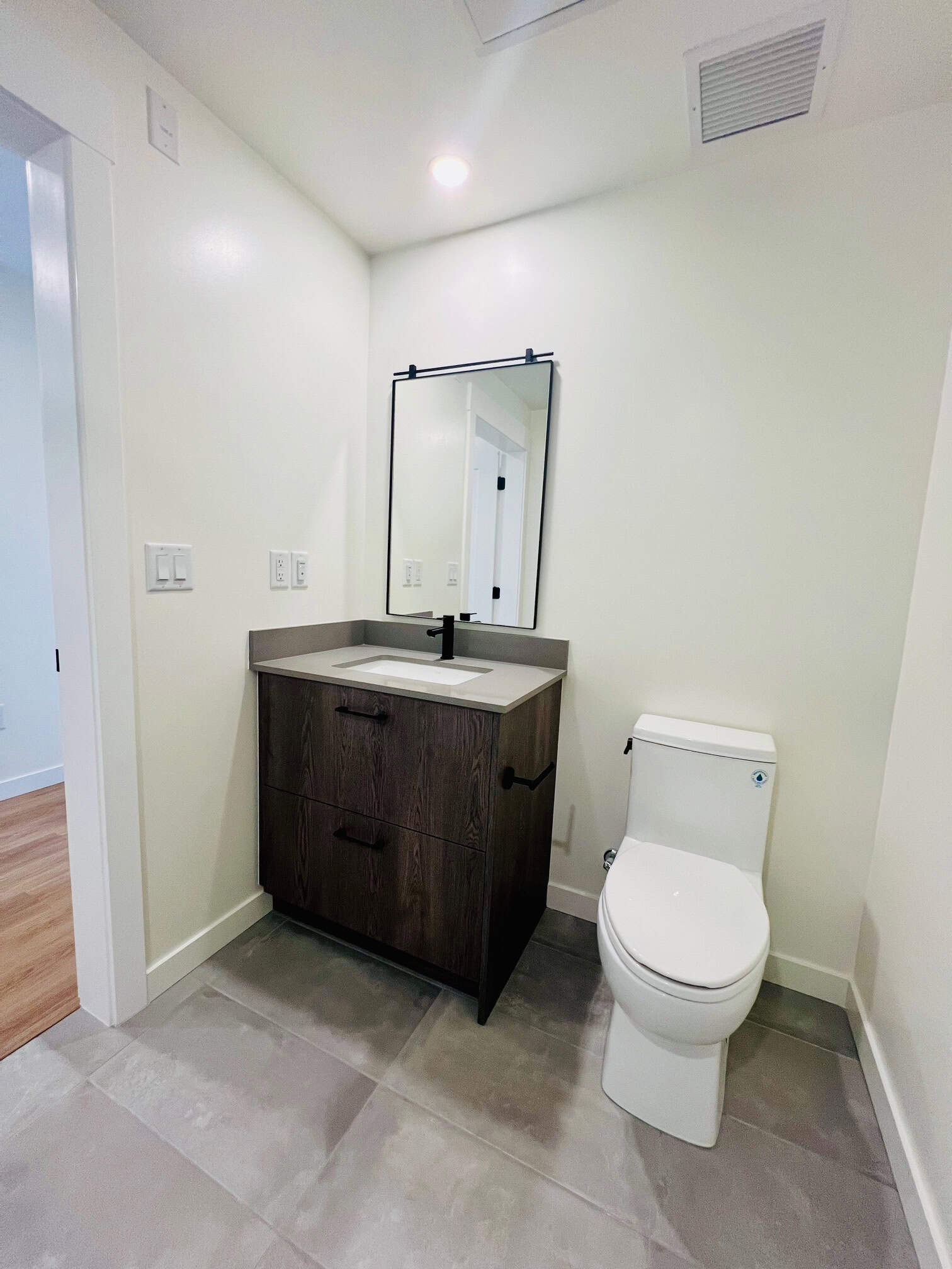 IMG_5604 Modern bathroom vanity with dark wood finish, white sink, black faucet, and sleek mirror with black frame, in a clean and contemporary space.