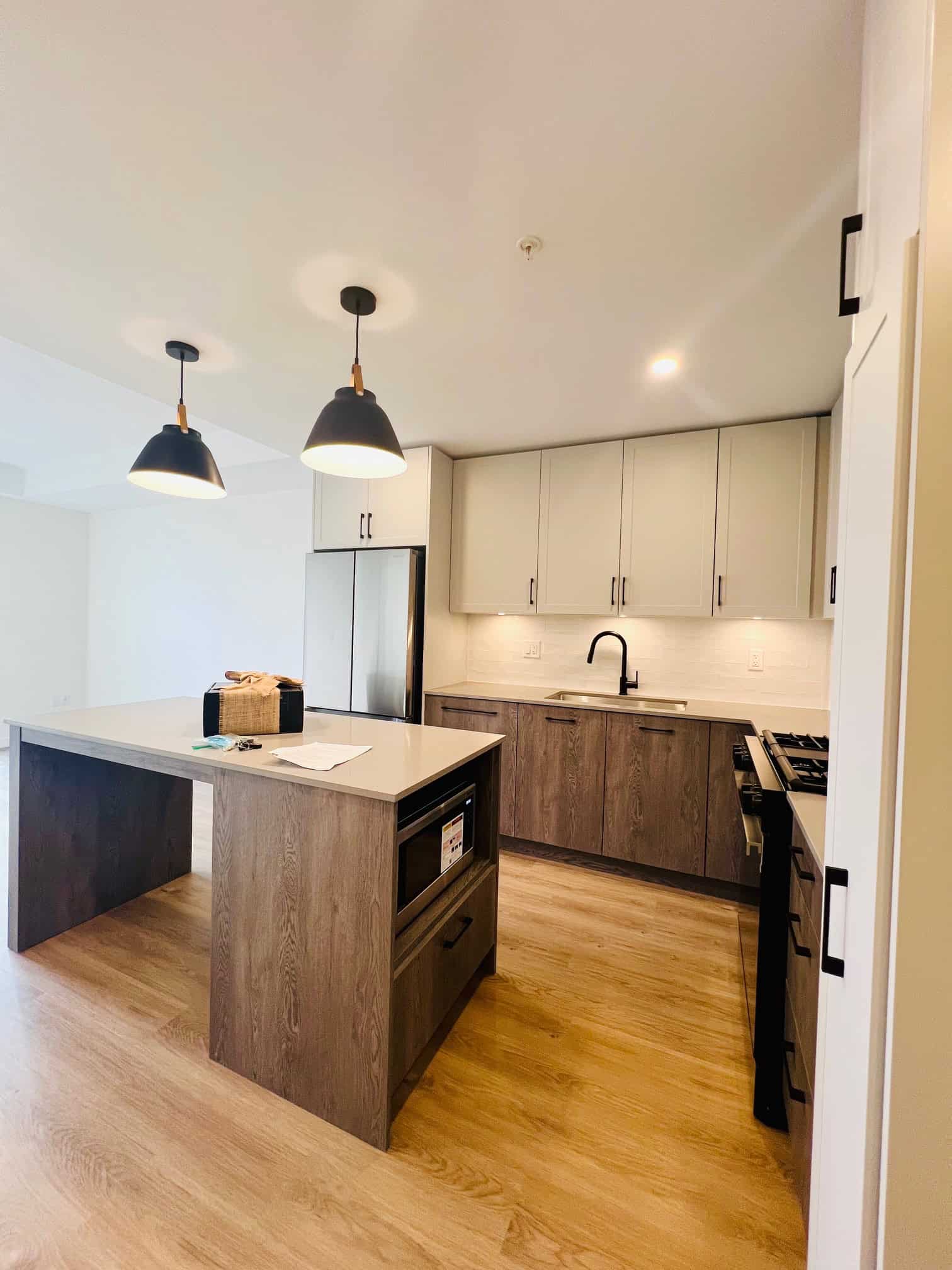 IMG_5606 Modern kitchen with white and wood cabinets, black fixtures, stainless steel appliances, and an island with built-in microwave - perfect Toronto-area home staging.