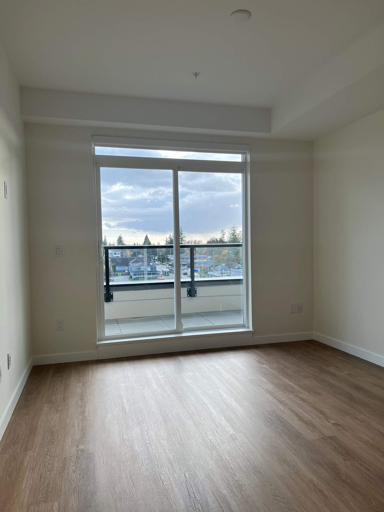 IMG_5608 Bright modern apartment with large sliding glass door opening to a balcony, featuring laminate flooring, neutral wall color, and scenic views, ideal for urban living and real estate investment in Vancouver.