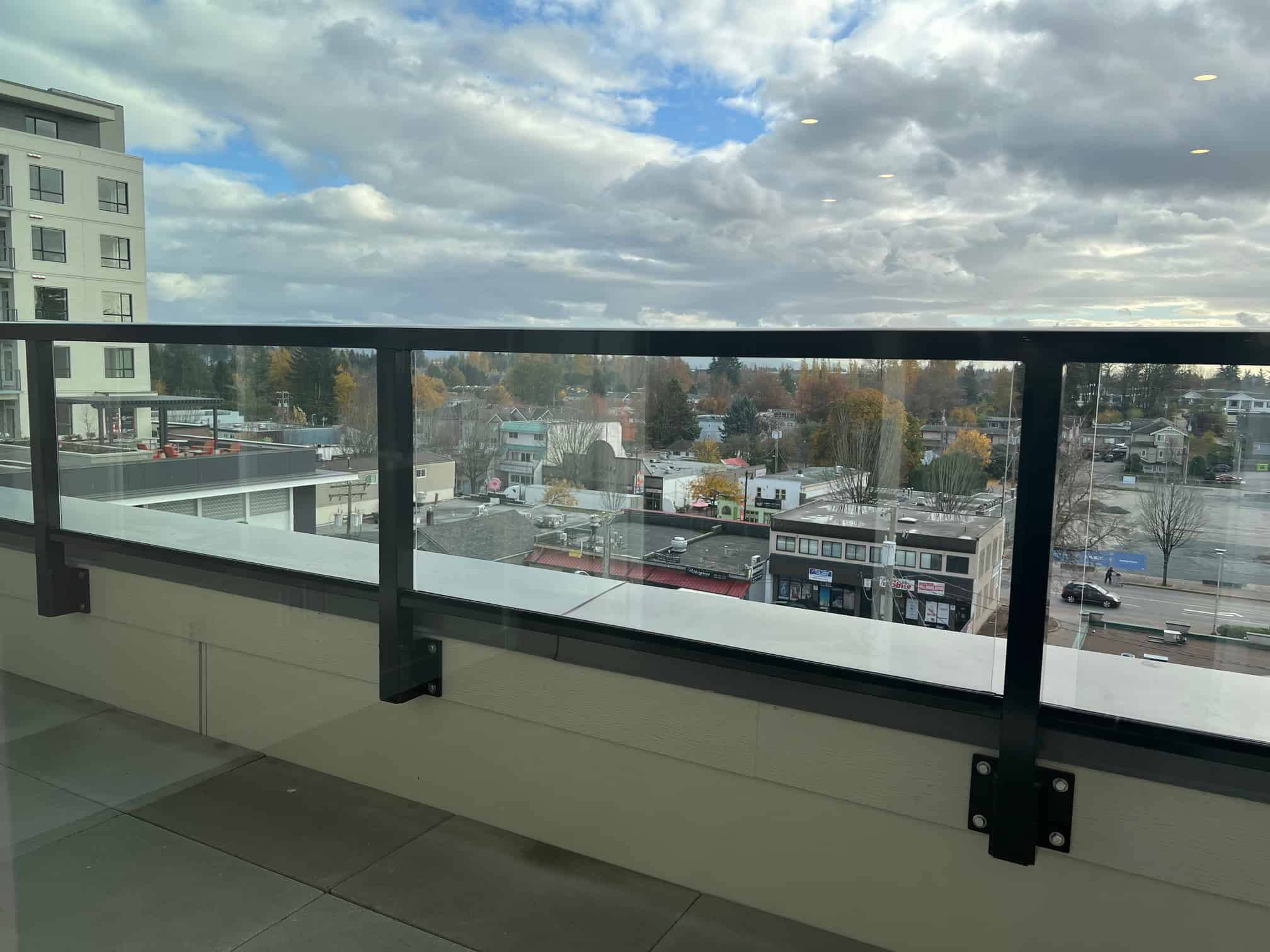 IMG_5609 Bright balcony view overlooking neighbourhood and commercial area with modern buildings, trees, and cloudy sky in Vancouver, BC, ideal for property presentations and real estate marketing.