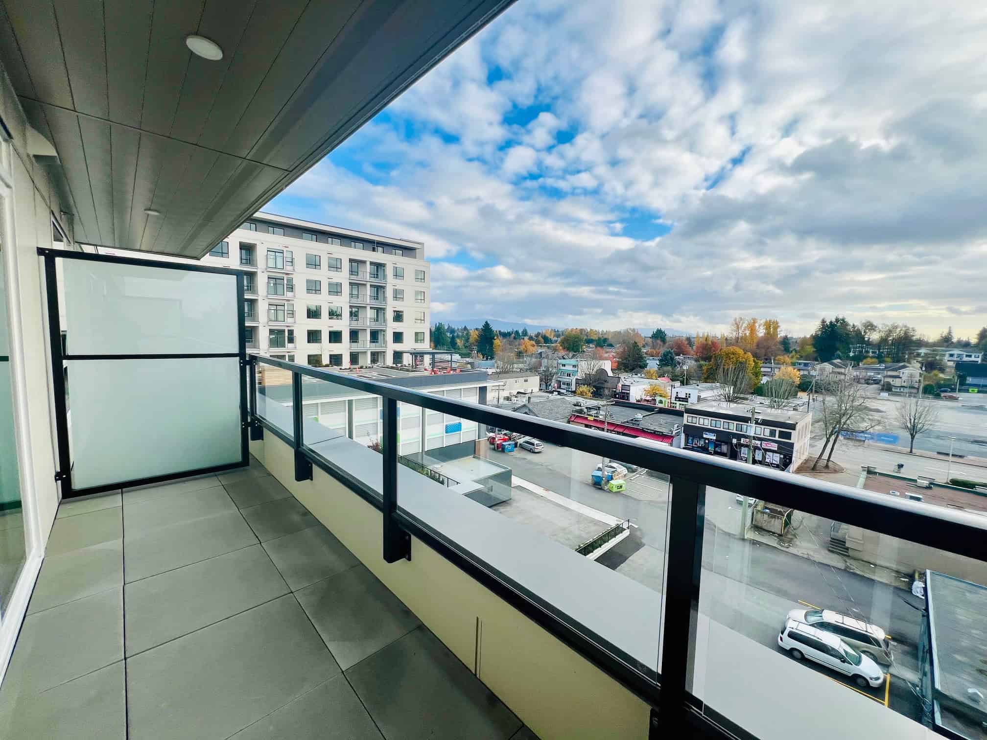 IMG_5612 Bright balcony view of urban landscape with modern residential and commercial buildings, colorful trees, and a partly cloudy sky in Vancouver, BC, showcasing the vibrant real estate market.