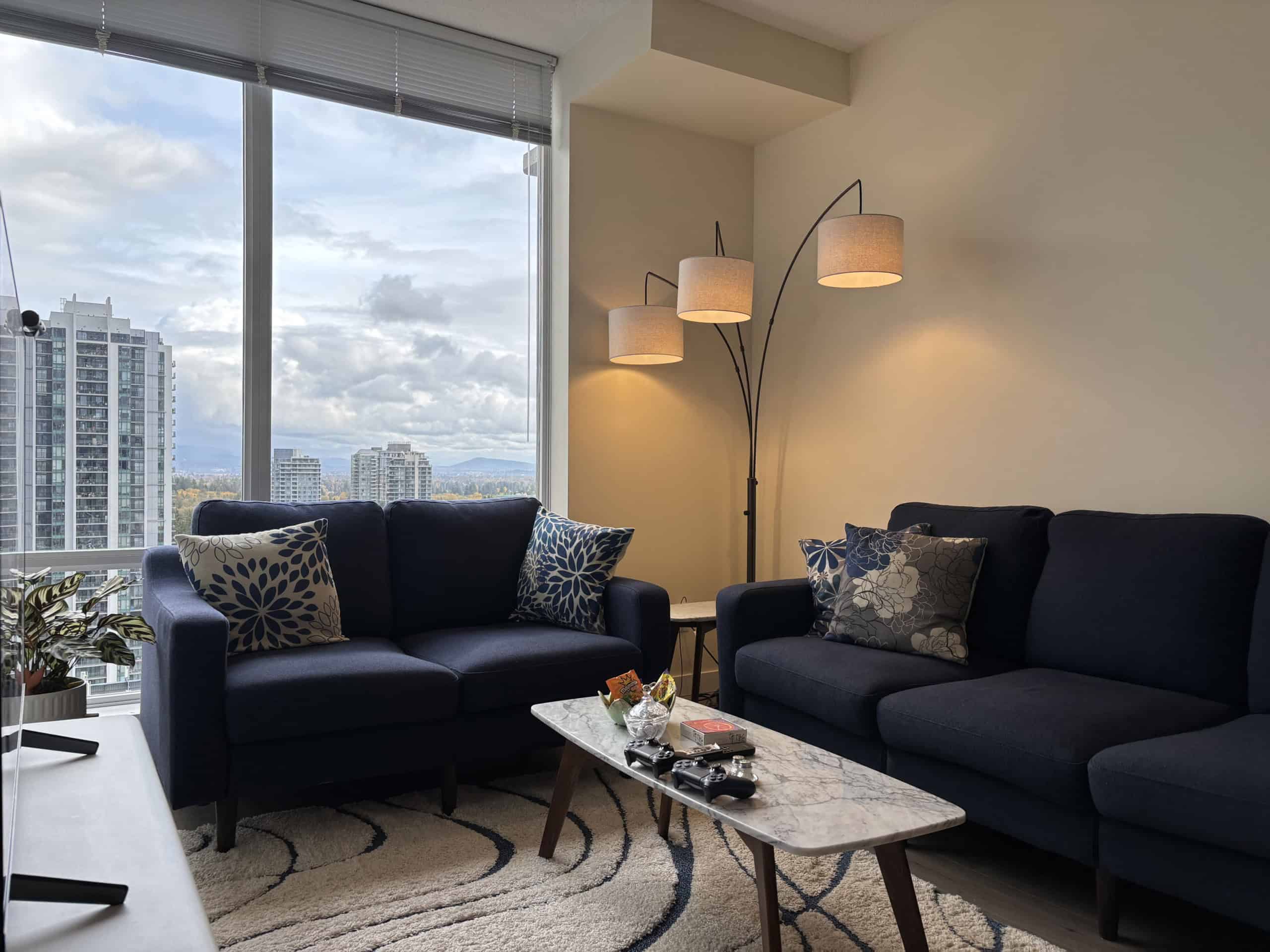Modern Vancouver high-rise apartment living with city views from large windows, stylish navy sofas, and cozy cozy decor perfect for real estate listings.