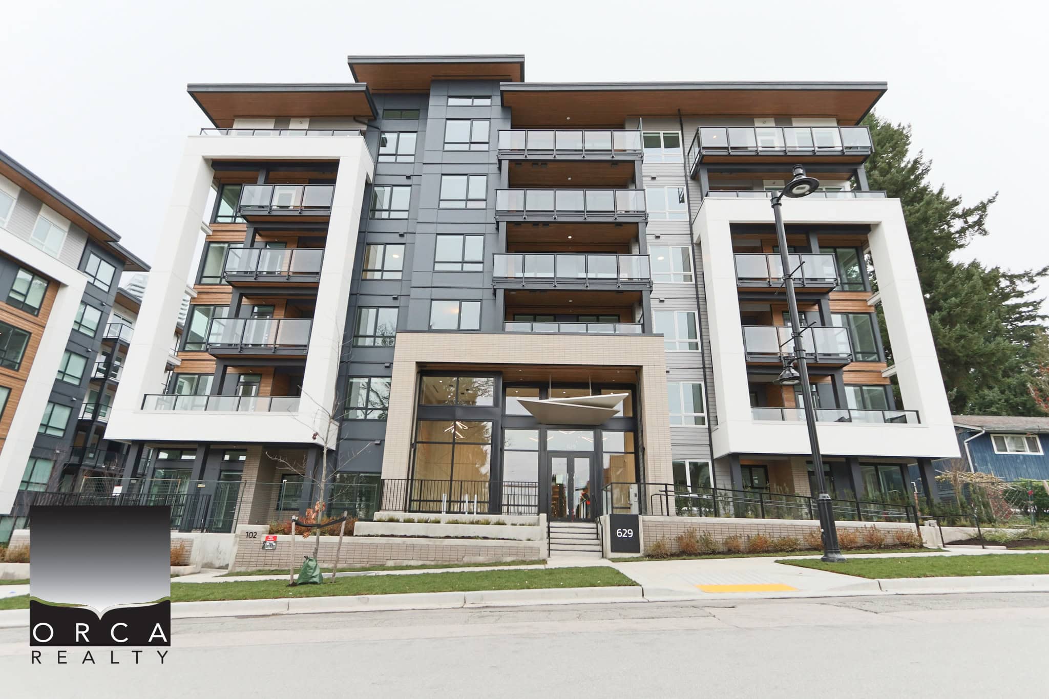Contemporary multi-story residential building with modern architecture, large glass balconies, and landscaped surroundings, representing prime Vancouver real estate by Orca Realty Inc.