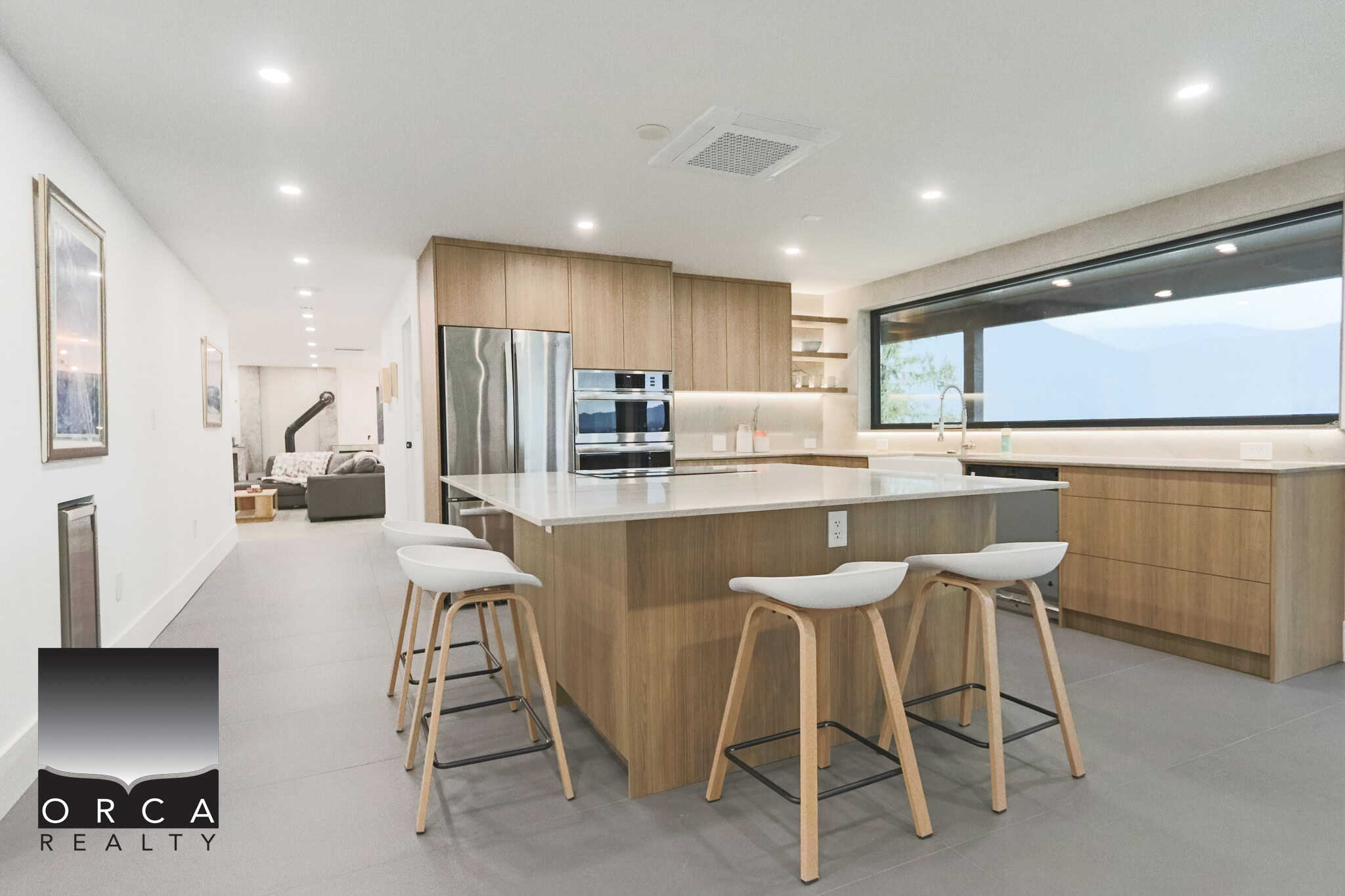 Bright modern kitchen with wooden cabinetry and large window, ideal for Vancouver Island homes, featuring stainless steel appliances and a spacious island with seating, perfect for real estate listings.