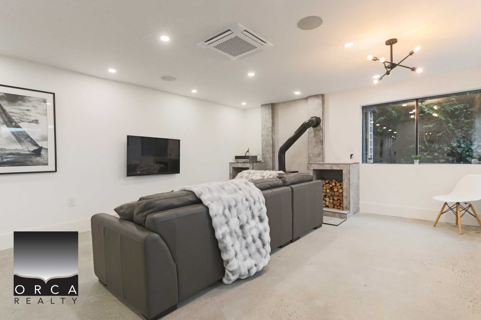 Cozy modern living room with a sleek grey sectional sofa, fireplace, and abundant natural light, showcasing Orca Realty Inc. luxury homes with stylish, functional interiors in Vancouver.