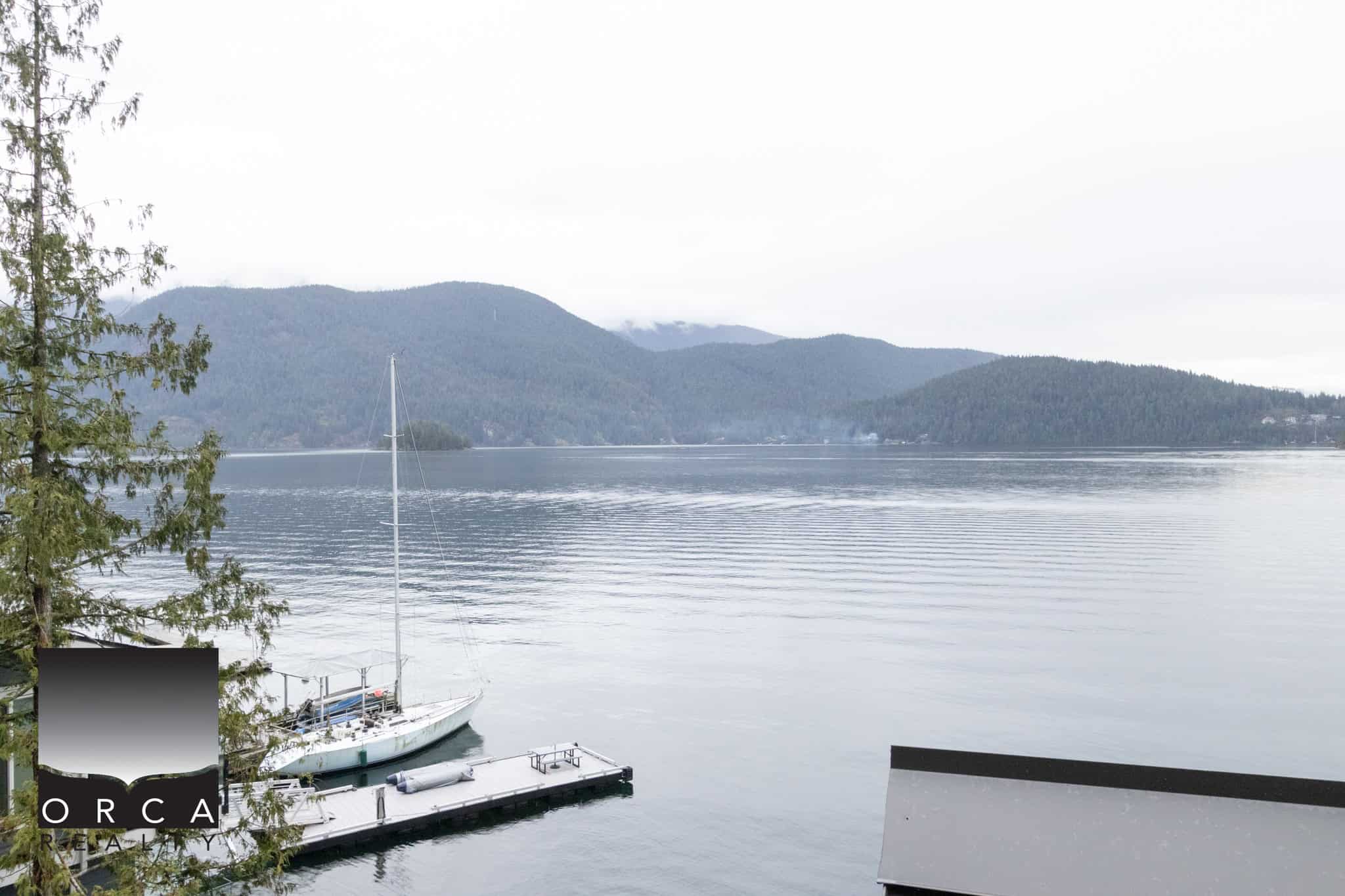 Serene waterfront view of a sailboat docked on calm waters with lush green mountains in the background, showcasing Orca Realty Inc.'s stunning property listings with scenic natural surroundings.