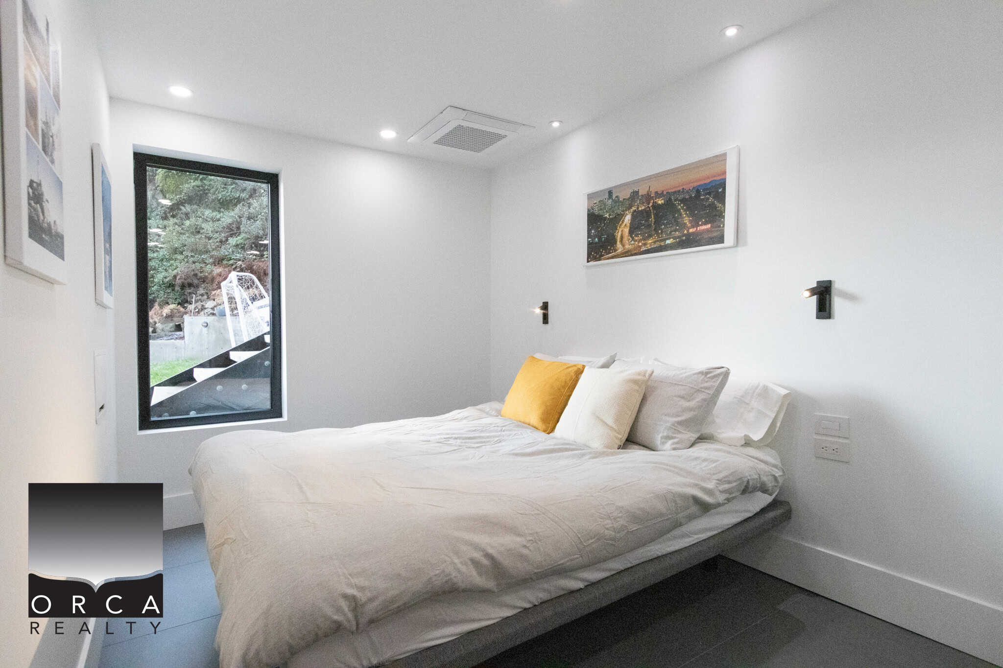 Modern bedroom with minimalist design, white walls, and cityscape artwork, featuring a large bed with white linens and accent pillows, ideal for Vancouver real estate listings.