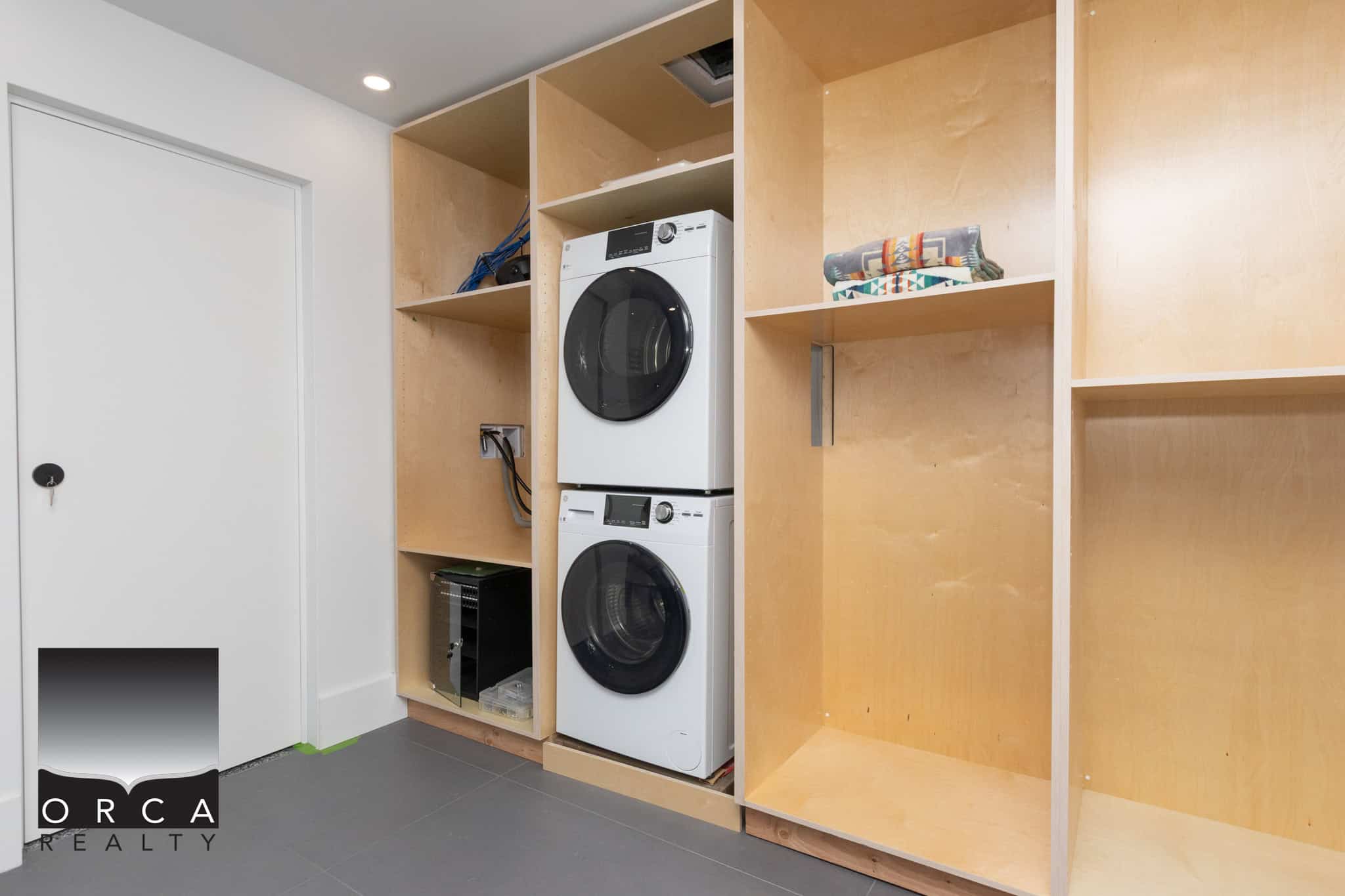 Stacked washer and dryer in a modern laundry room with custom shelving and storage space. Ideal for home organisation and laundry convenience in a contemporary Canadian home.