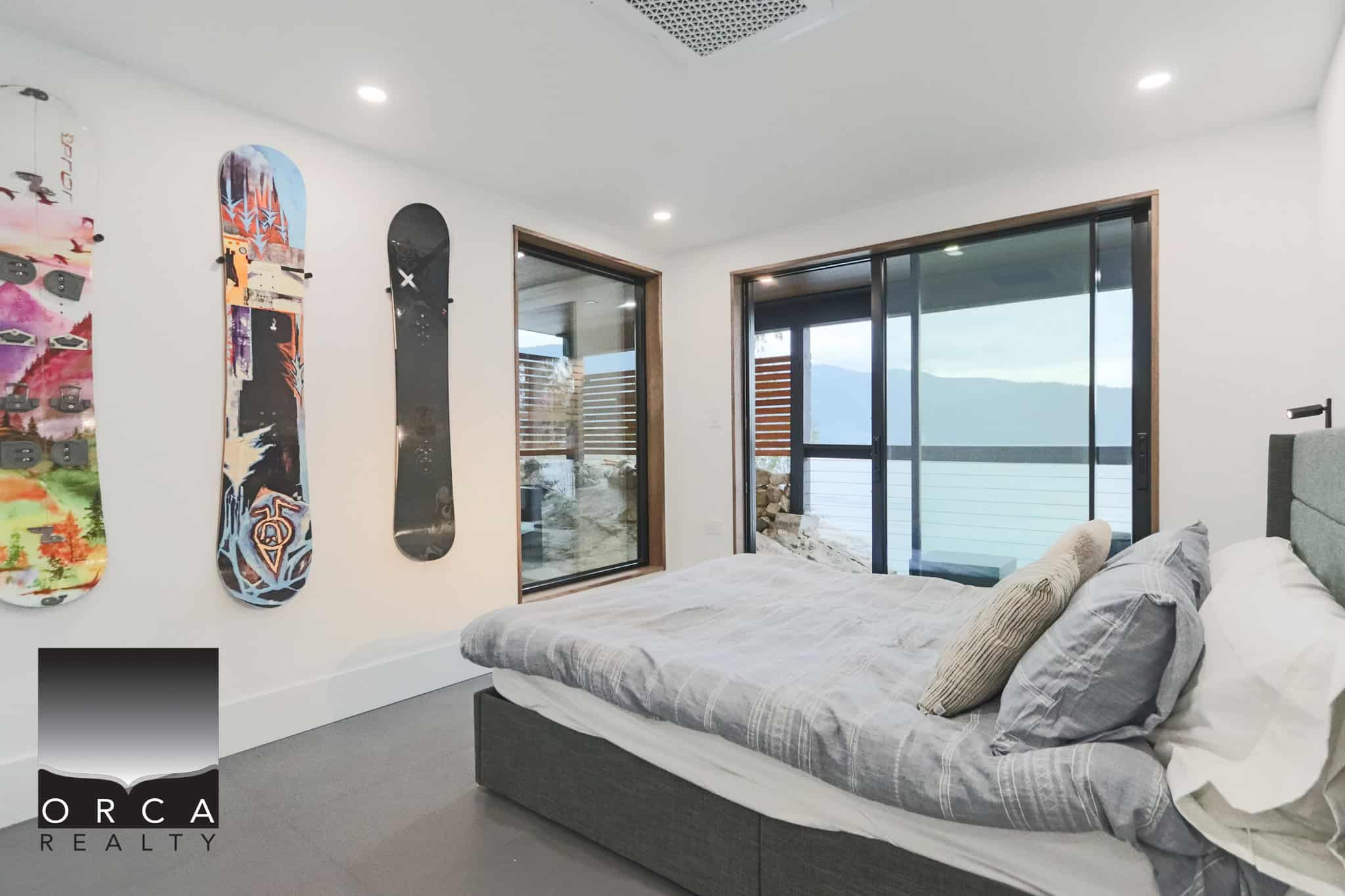 Waterfront bedroom with mountain view, modern decor, large sliding glass doors, Orca Realty listing, coastal living, mountain scenery, ocean view, bright interior, luxury home, real estate Vancouver Island Canada.