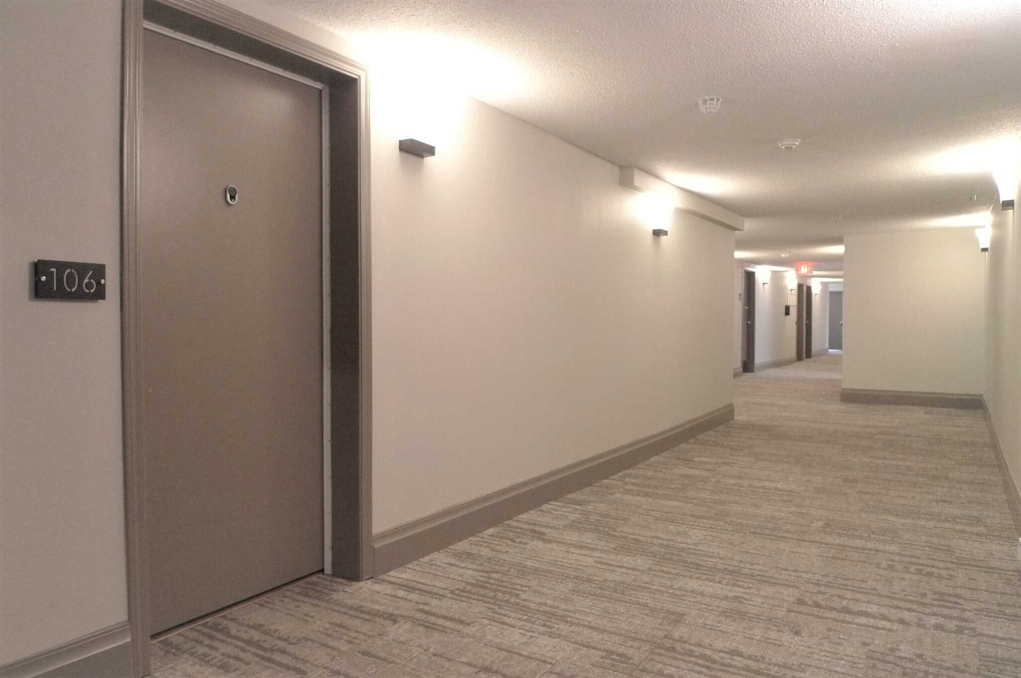 Bright and modern apartment hallway at Orca Realty Inc. with clean white walls, carpeted flooring, and contemporary wall sconce lighting, showcasing professional property management services in Vancouver.