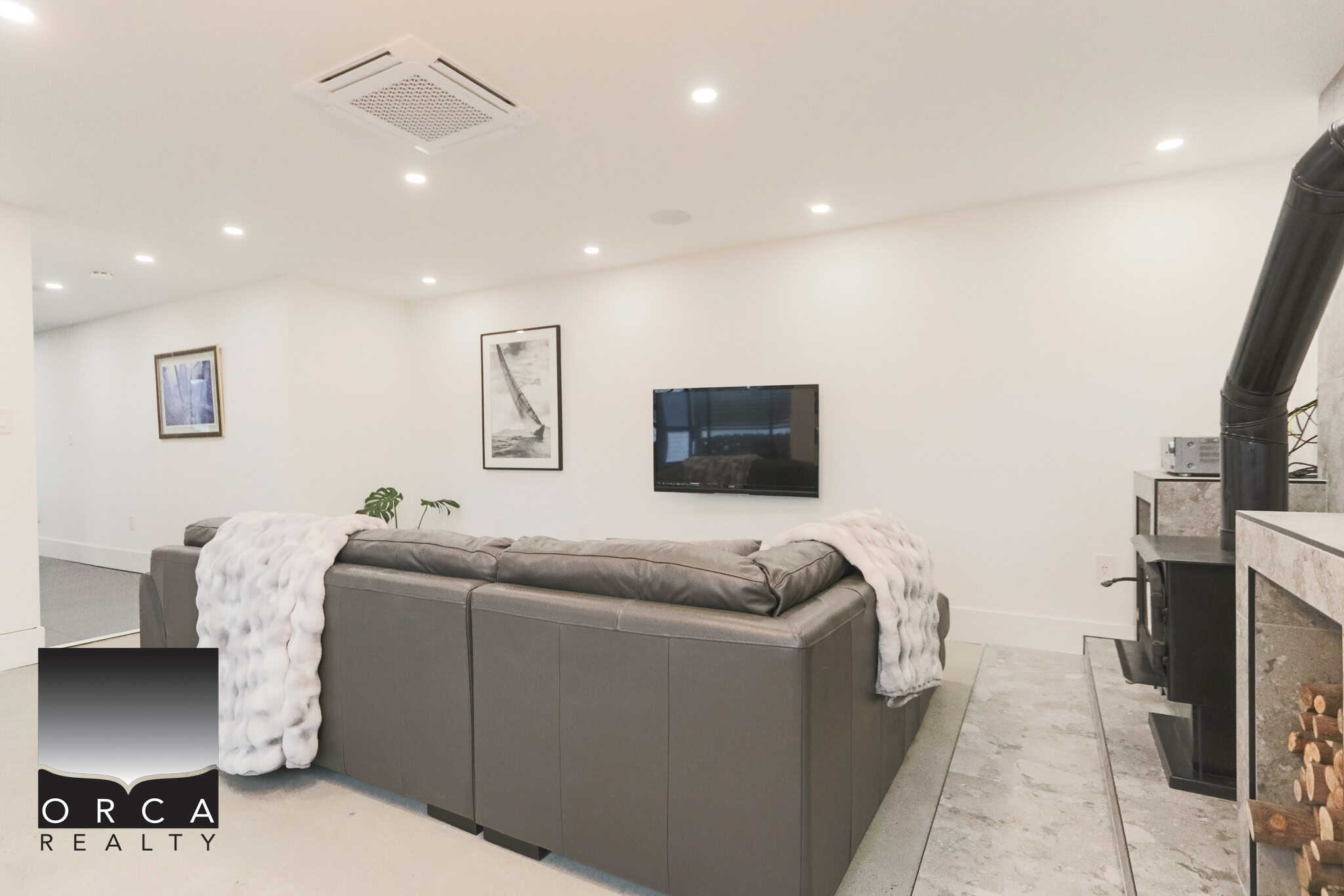 Cozy modern living room featuring a large sectional sofa, fireplace, and wall-mounted TV, perfect for relaxing in an upscale residential property listed by Orca Realty Inc.