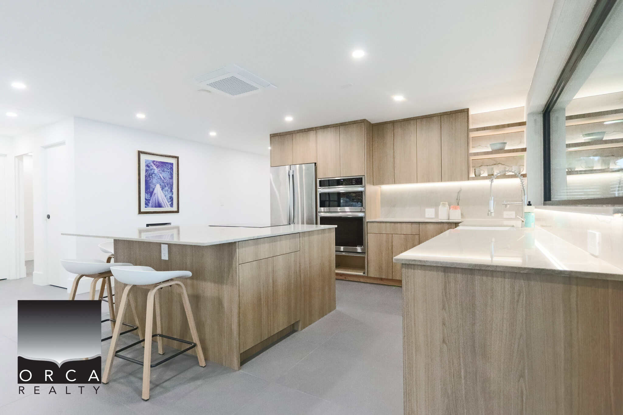 Modern kitchen with wood cabinetry, marble countertops, stainless steel appliances, ample storage, and bright lighting, ideal for Vancouver Island real estate buyers.