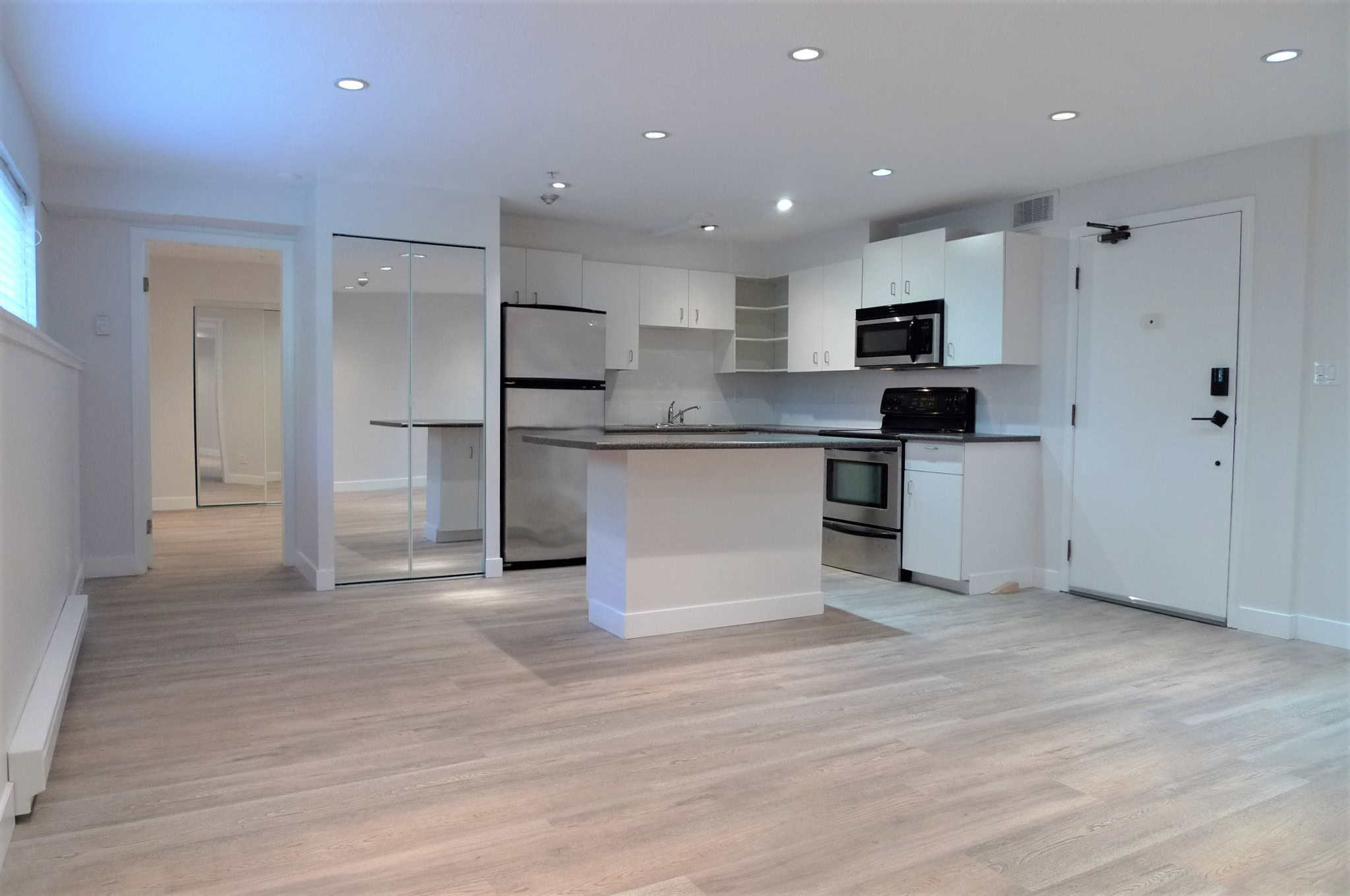 Bright modern kitchen with white cabinets, stainless steel appliances, and laminate flooring, ideal for Vancouver Island real estate buyers seeking stylish homes via Orca Realty Inc.