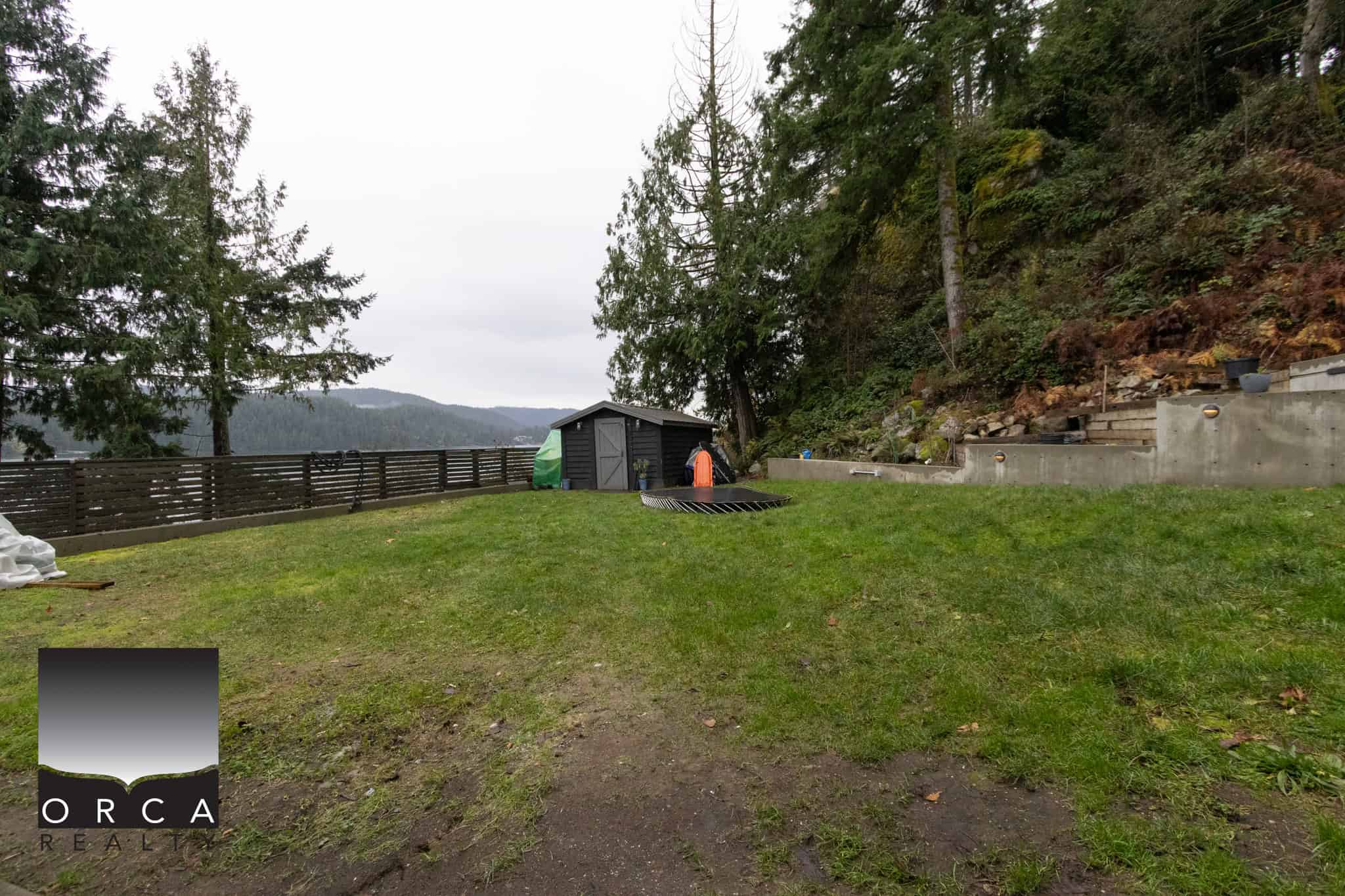 Spacious backyard with lush green lawn, outdoor shed, and scenic views of trees and mountains, perfect for Vancouver Island real estate and waterfront property investments.