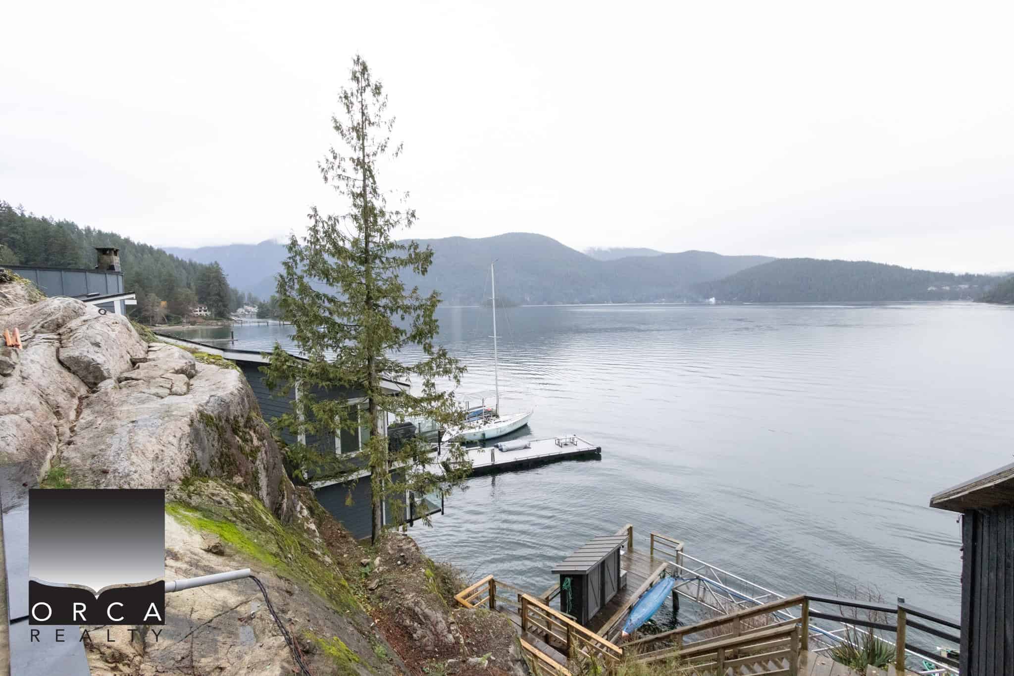 Serene waterfront property with a dock, sailboat, and scenic mountain views on Vancouver Island, BC; ideal for luxury real estate and waterfront homes in the Orca Realty portfolio.
