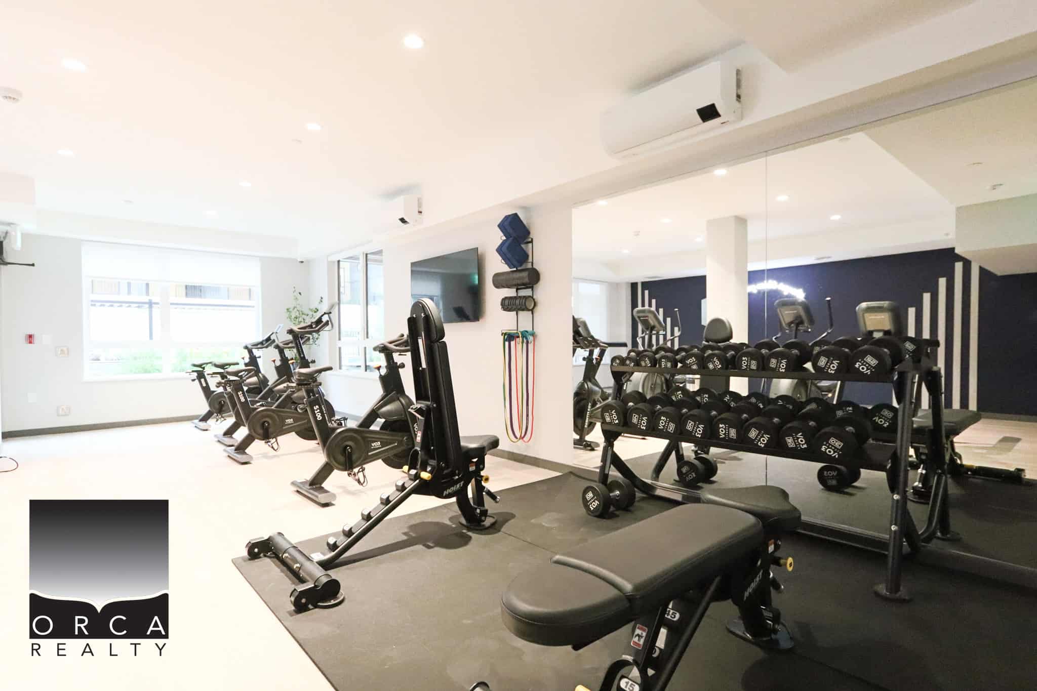 23 Modern indoor fitness centre with advanced gym equipment, free weights, and cardio machines at Orca Realty Inc., ideal for maintaining active lifestyle in Vancouver's real estate market.