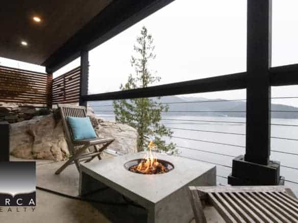 Stunning waterfront balcony with modern fire feature, wooden lounge chairs, and panoramic water views, perfect for relaxing in Victoria BC.
