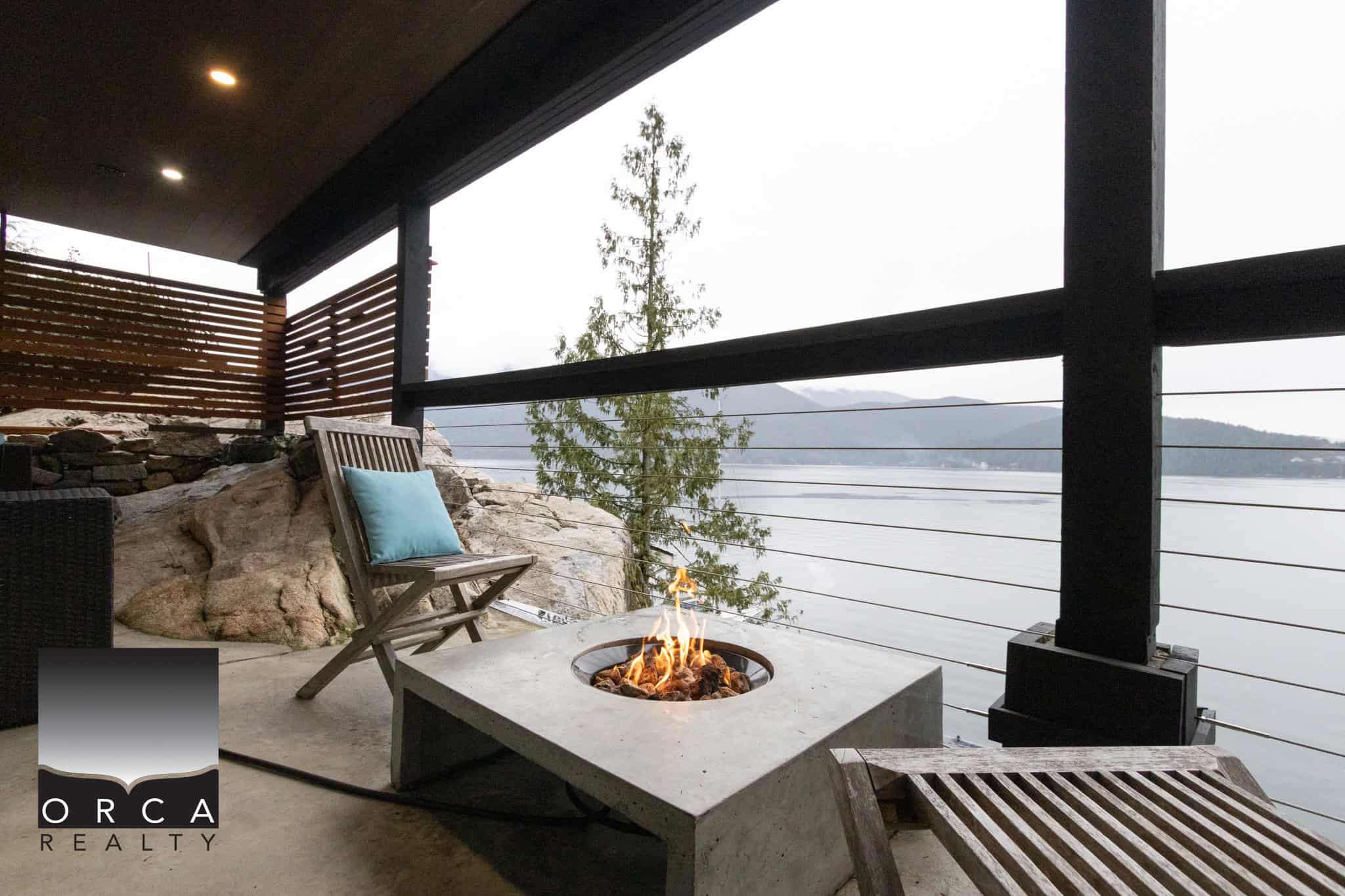 Stunning waterfront balcony with modern fire feature, wooden lounge chairs, and panoramic water views, perfect for relaxing in Victoria BC.
