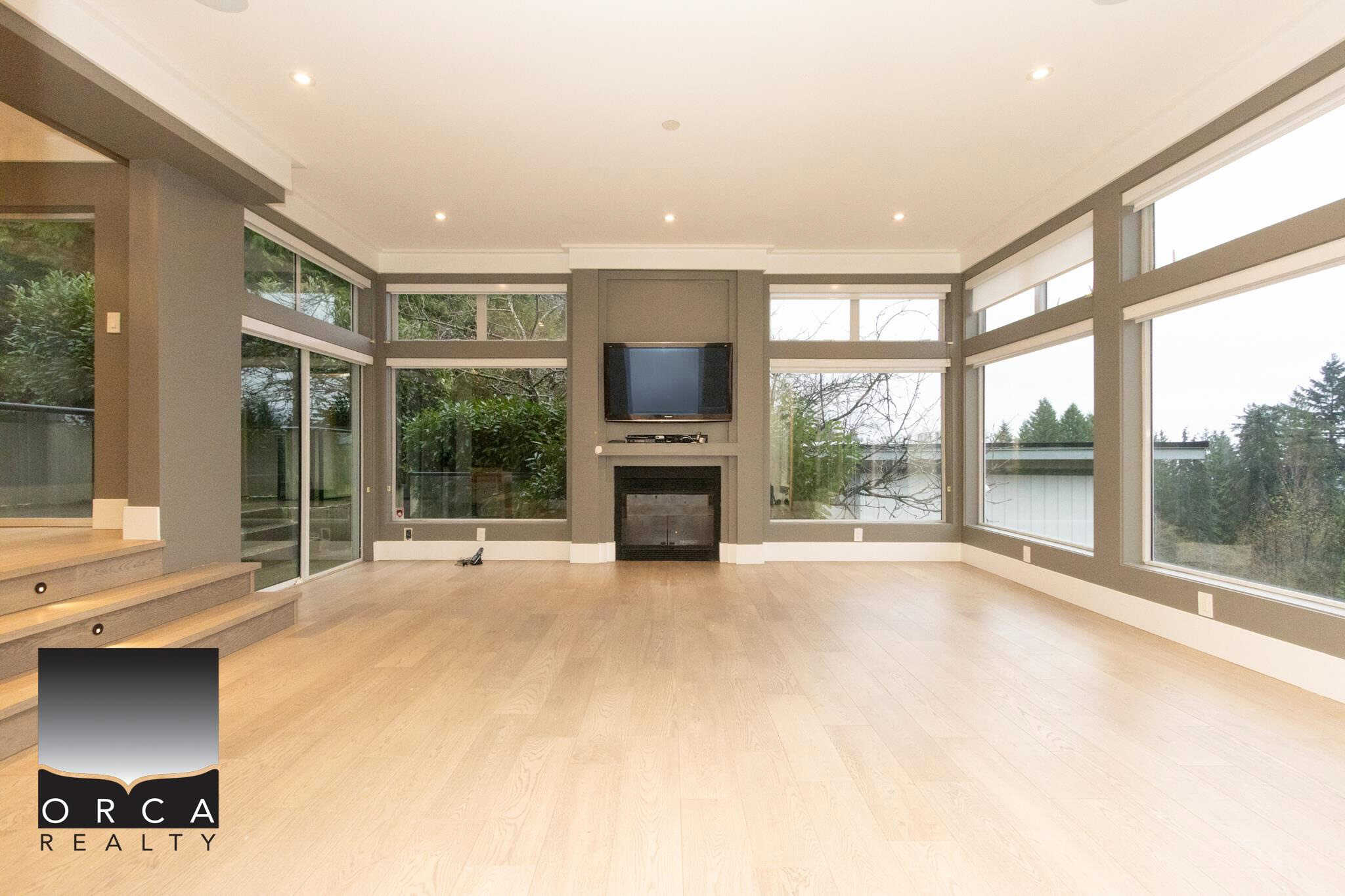Bright modern living room with large windows, hardwood flooring, and a cozy fireplace, perfect for relaxing and entertaining in a scenic Vancouver home.