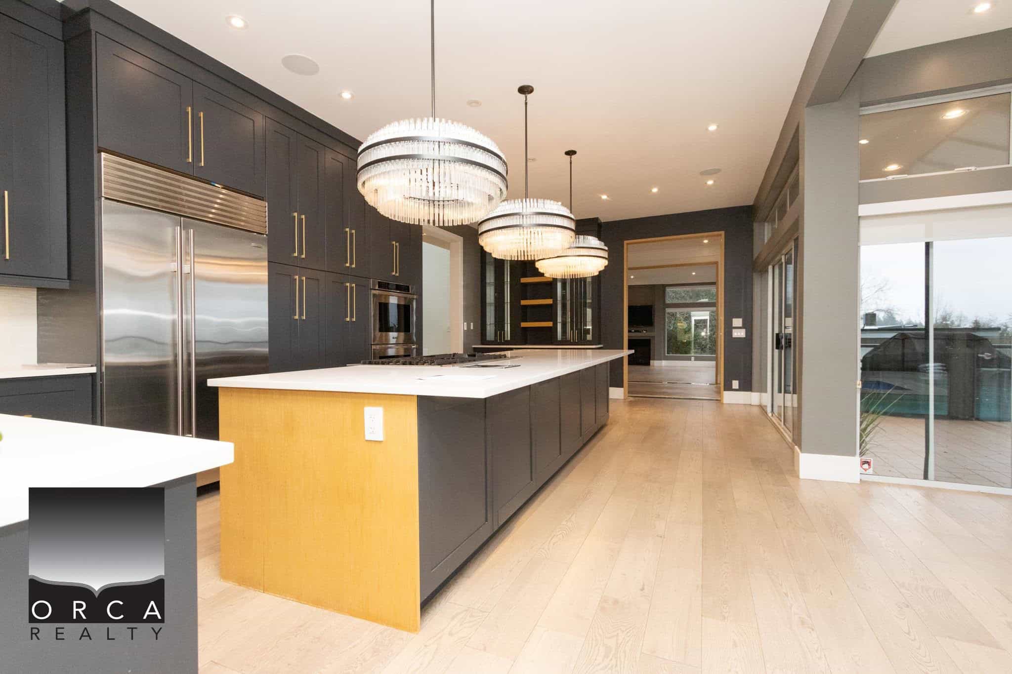 Stunning modern kitchen with sleek black cabinetry, island with white countertop, pendant lighting, and expansive glass doors offering natural light and outdoor views.