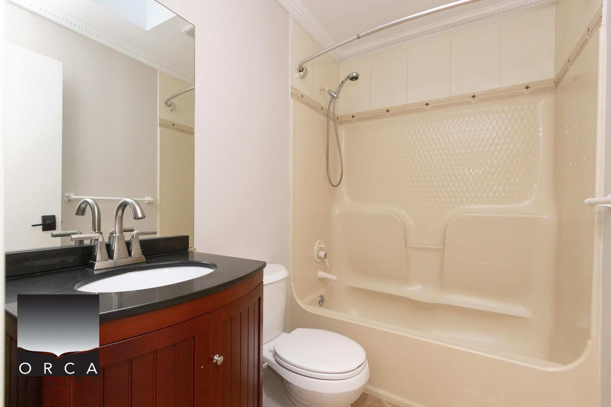 Clean modern bathroom with bathtub, shower, vanity with black countertop, and toilet, showcasing high-quality real estate features perfect for Toronto and GTA homes.