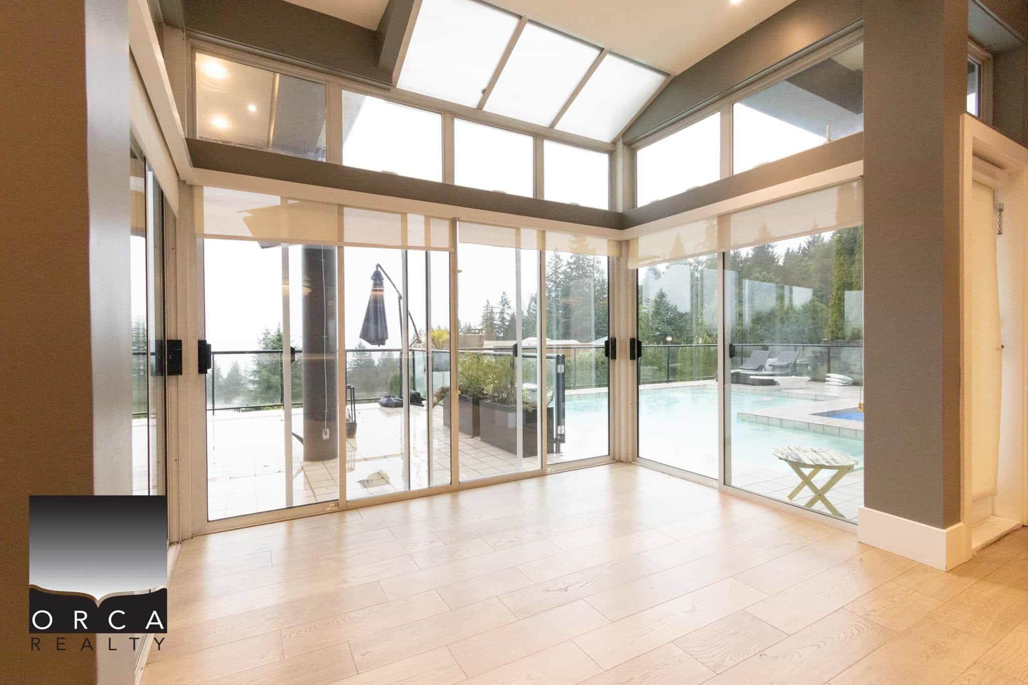 Bright sunroom with large glass sliding doors opens to pool and deck area, offering a perfect indoor-outdoor living space with beautiful views and natural light.